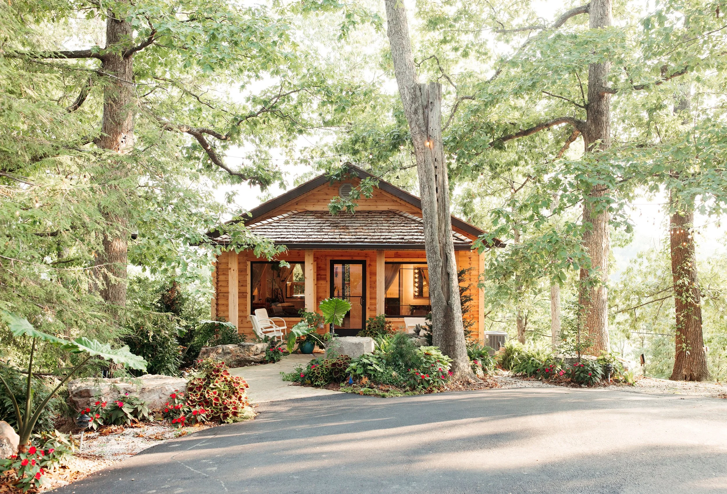 Small wooden house in a forested area with trees and colorful flowers in the garden.