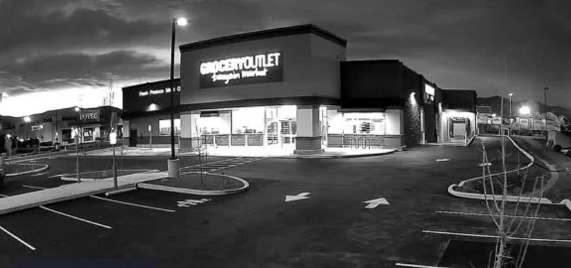Empty parking lot outside a large retail store during dusk with minimal lighting and no cars.