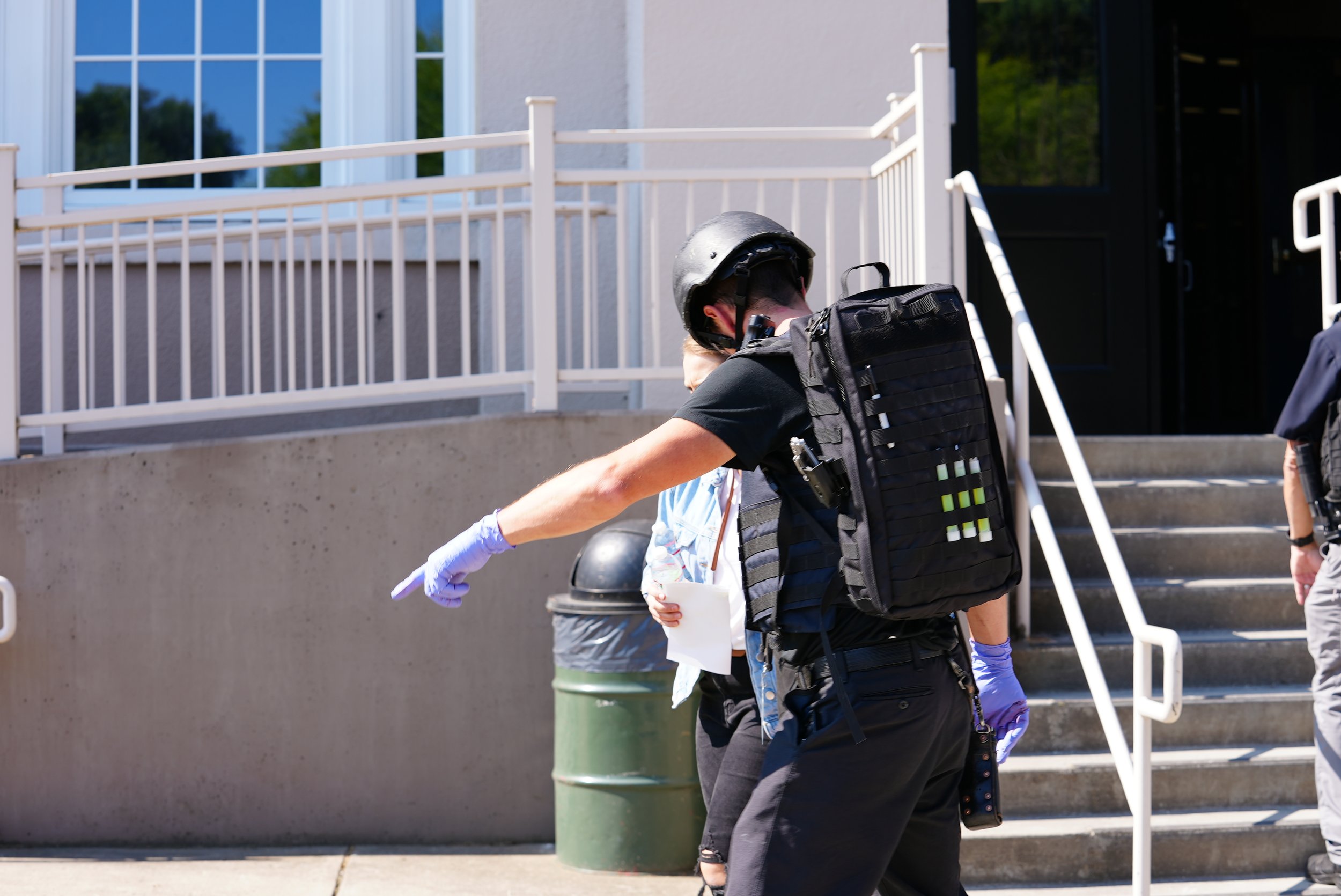 Police officer pointing while talking to a person outside a building with stairs and large windows.