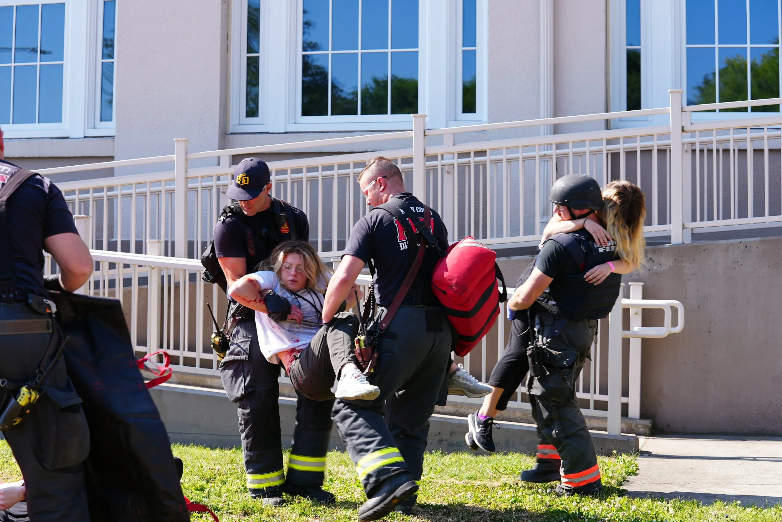 Emergency rescue personnel carrying a young girl with a head injury away from a building.