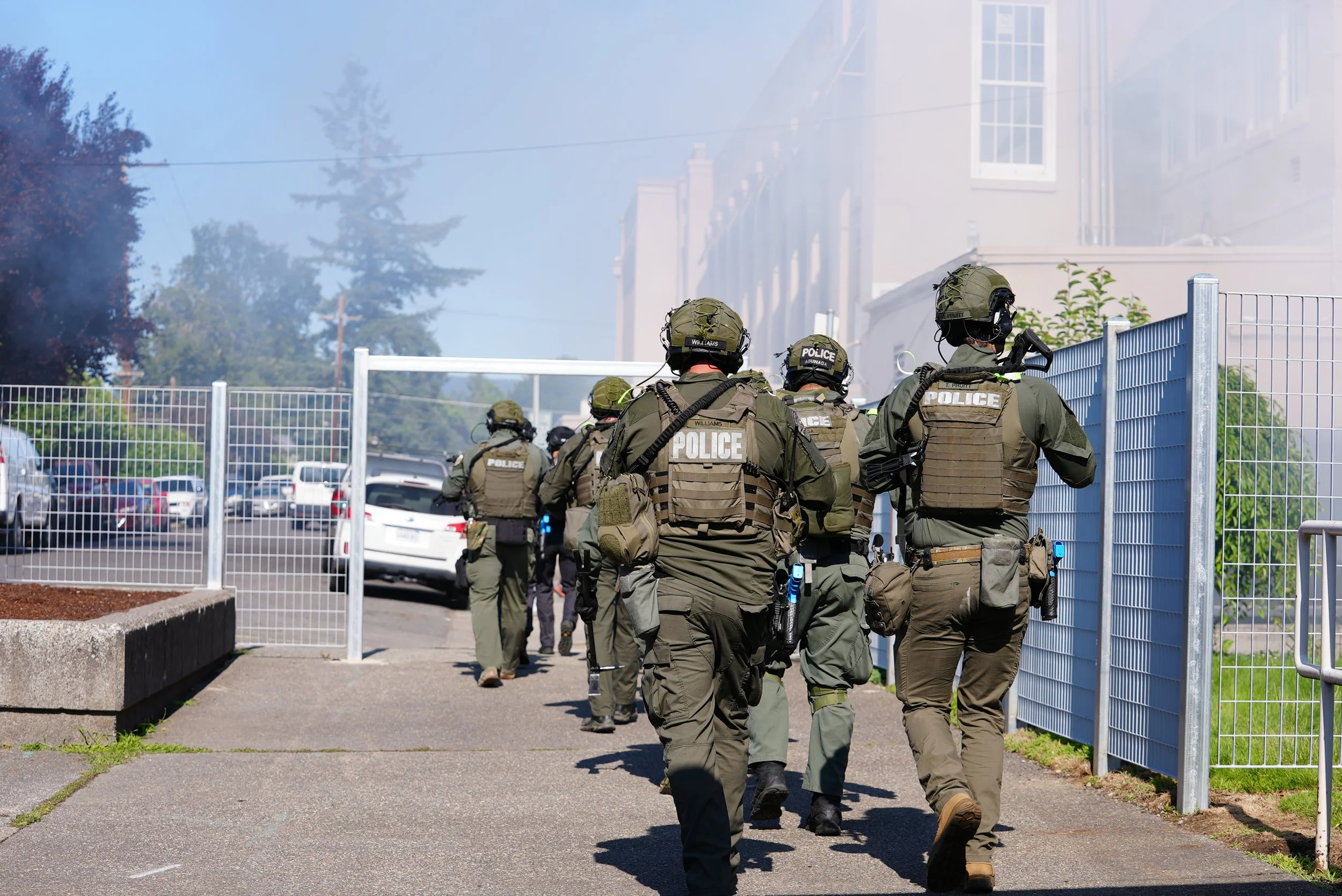 A group of police officers in tactical gear walking towards a building at a protest or emergency scene.