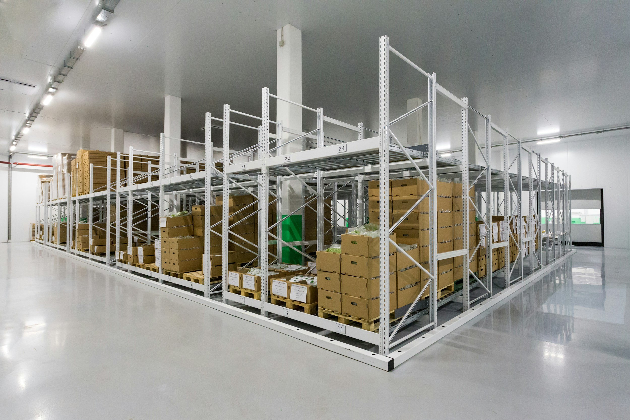 Empty warehouse with metal shelving units filled with cardboard boxes stacked on pallets.