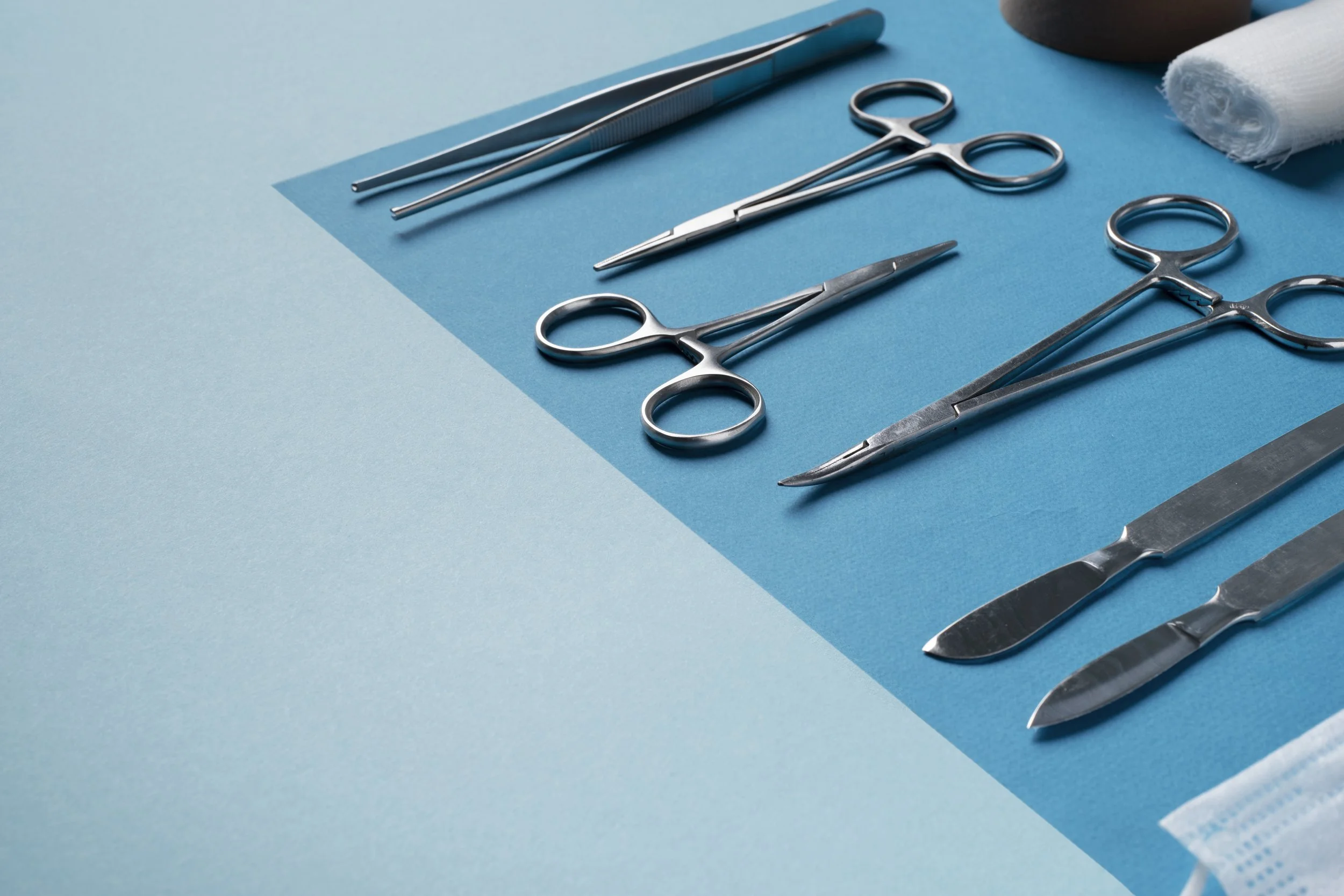 Set di strumenti chirurgici metallici su un piano di lavoro con sfondo blu.