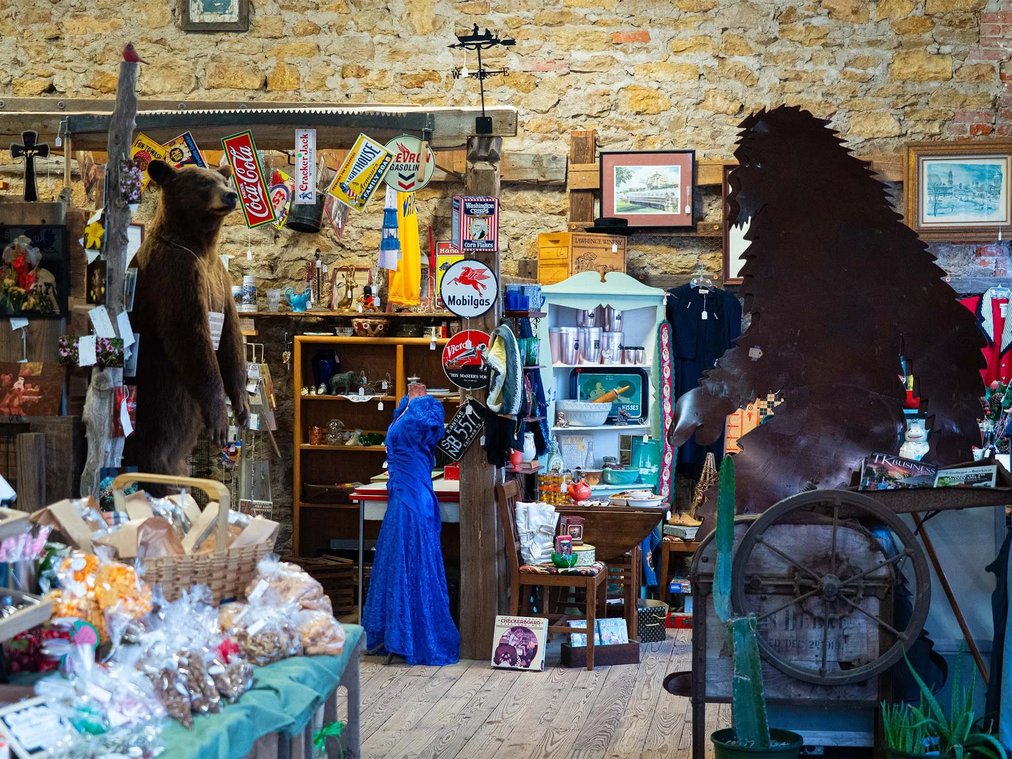 Interior of a vintage thrift store with various knickknacks, signs, and memorabilia, including a bear and a large monster or dinosaur statue.