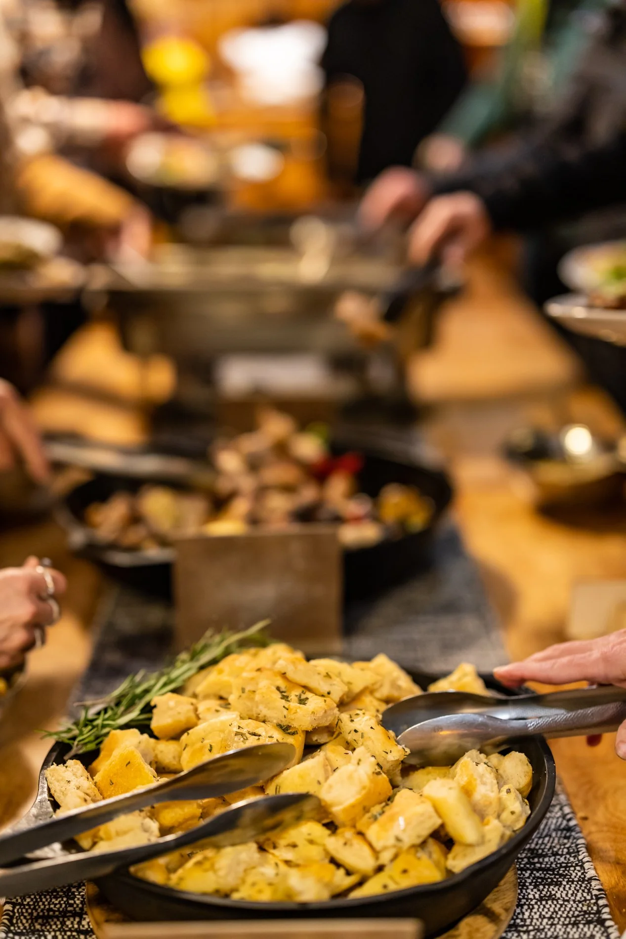 Close-up of a serving dish filled with seasoned, roasted potatoes garnished with fresh herbs at a buffet table.