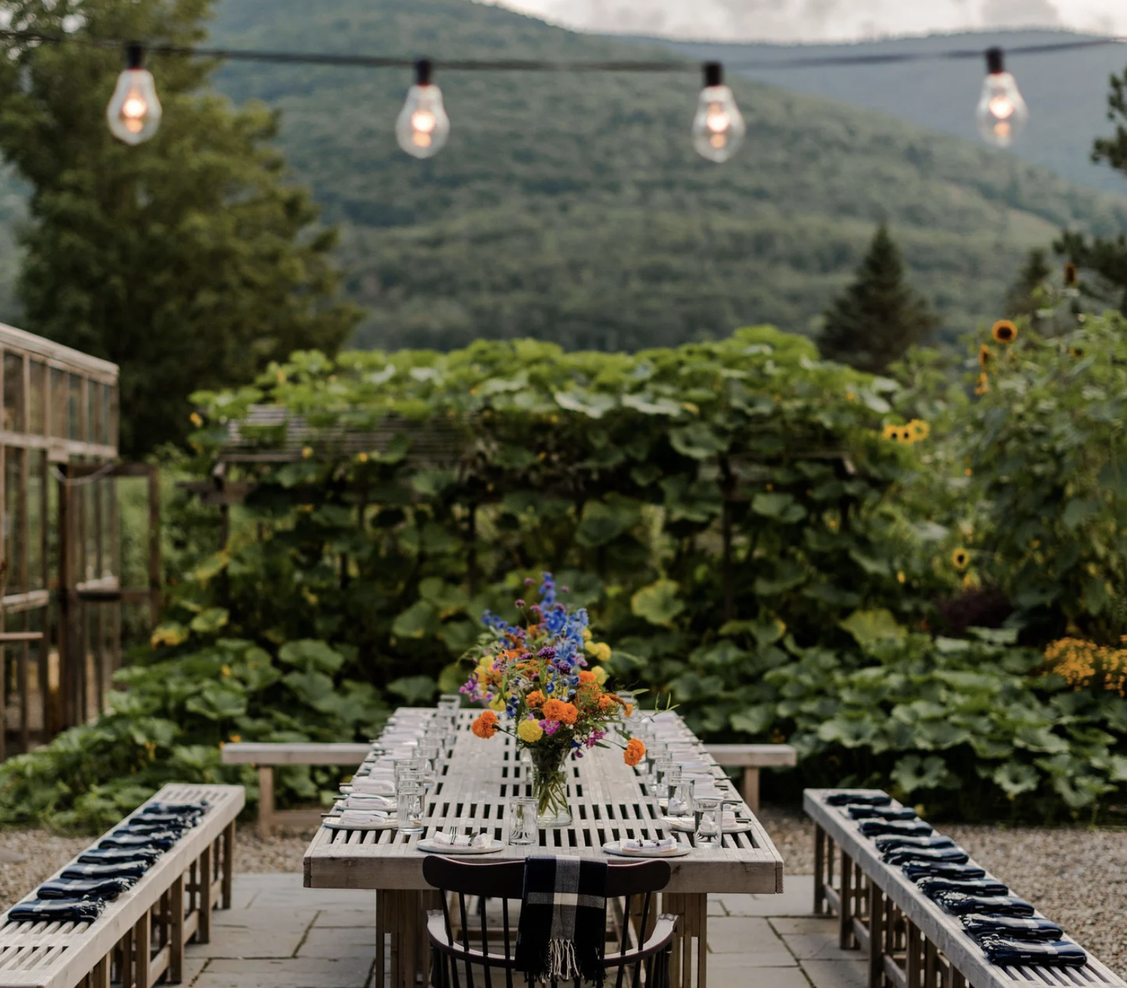 Person sitting on a rock by a calm river in a forested area with mountains in the background.
