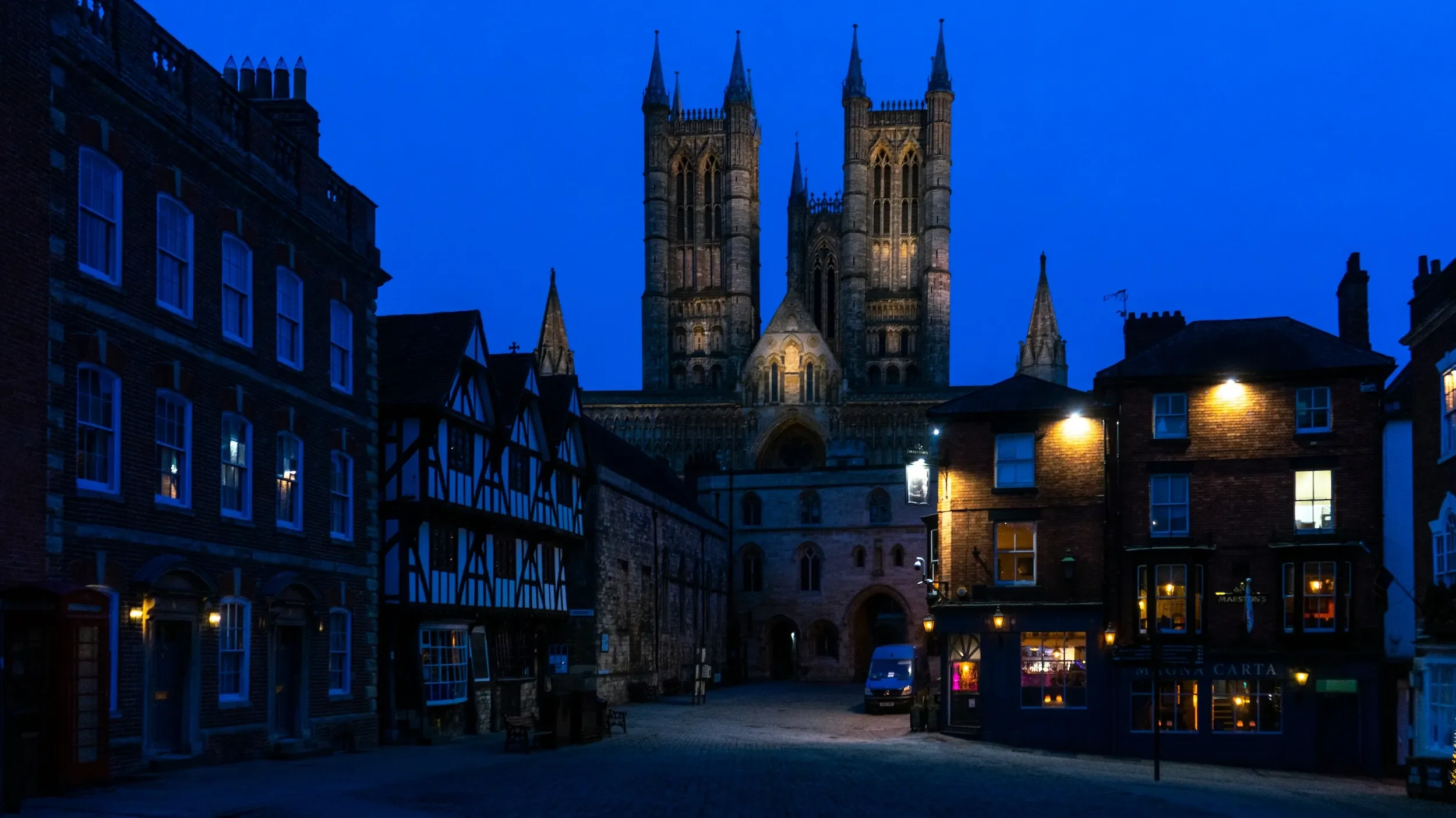 Nighttime view of Lincoln Cathedral above historic brick and timber buildings, under a dark blue sky.