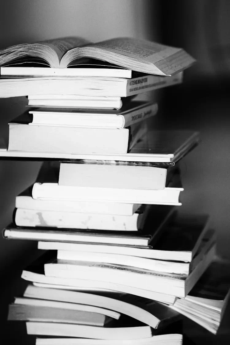 A stack of open and closed books, with one open book placed on top in black and white.