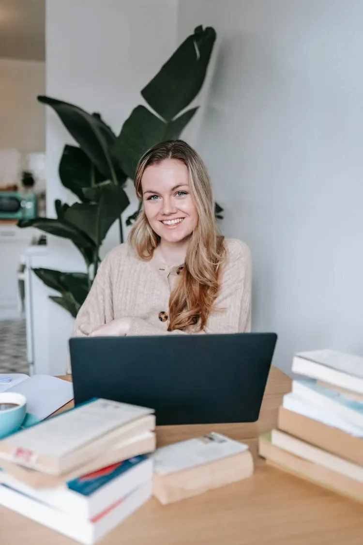 A counselling student smiling sitting at a desk with books and a laptop