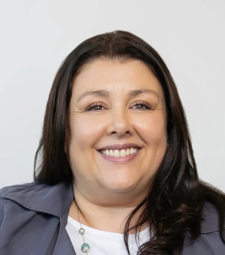 A smiling woman with dark hair, wearing a blazer and necklace, against a plain light background.