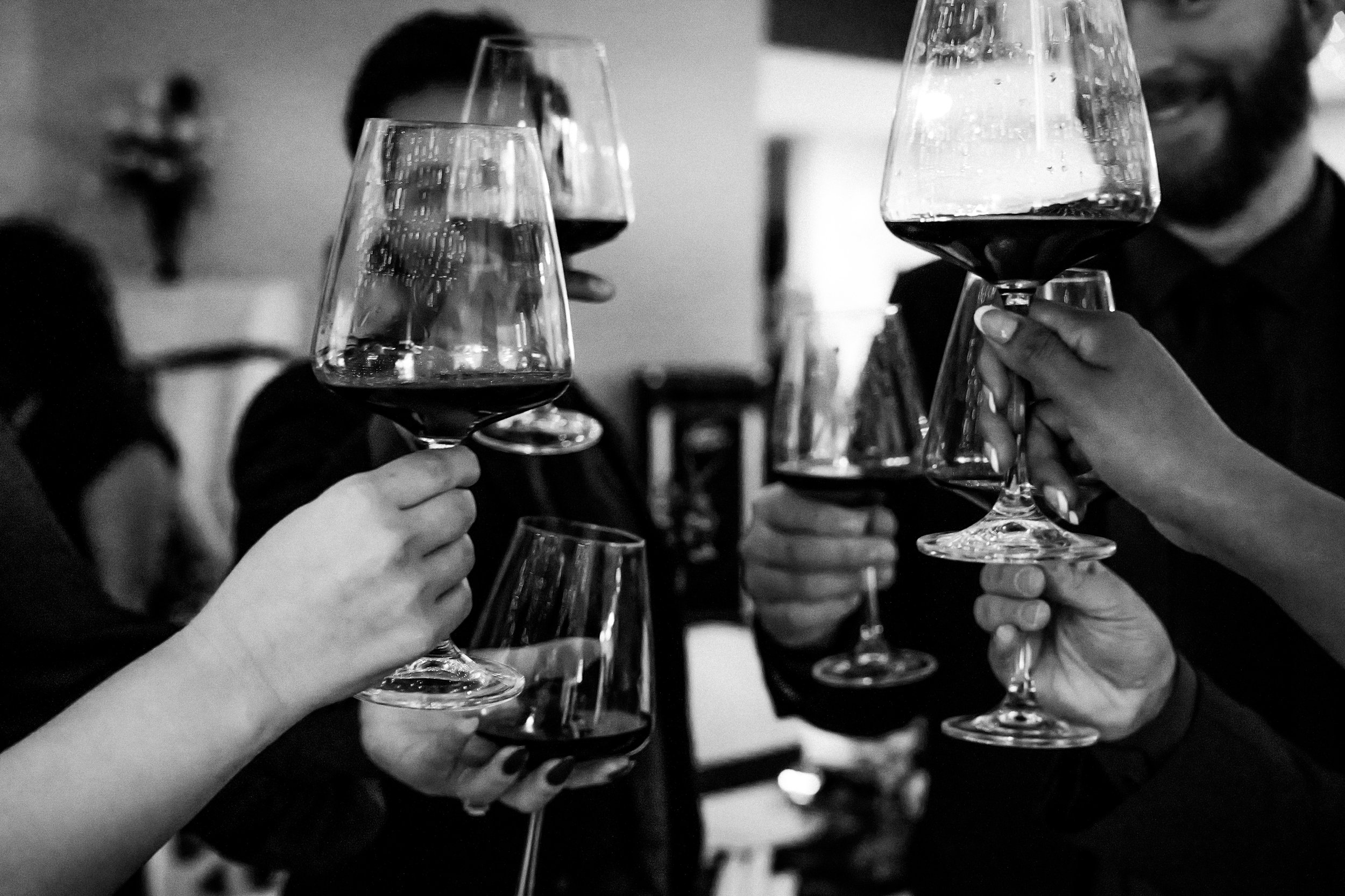 People clinking glasses of red wine in a celebratory toast at a social gathering.