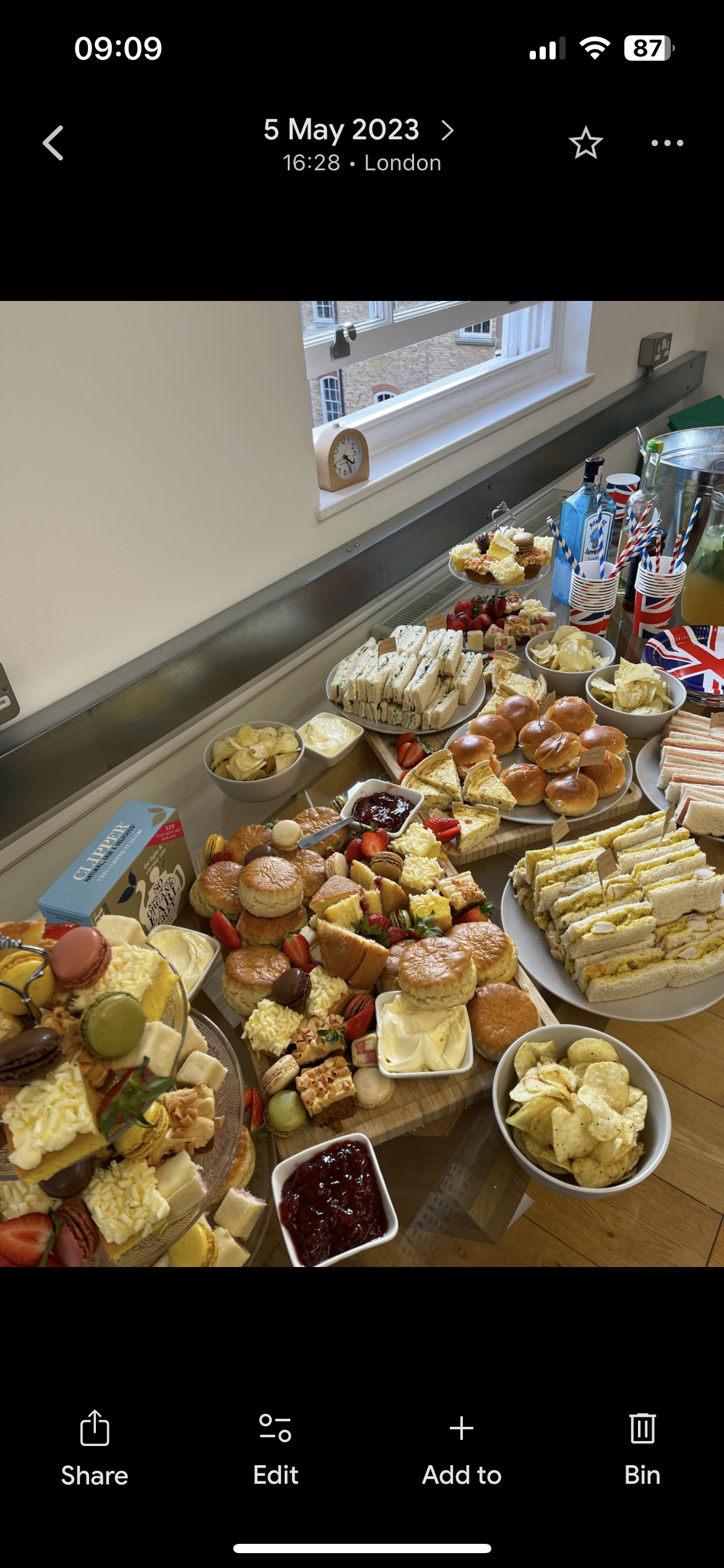 A table filled with various snacks and desserts, including sandwiches, mini burgers, cupcakes, cookies, strawberries, chips, and various beverages, all arranged for a celebration or gathering.