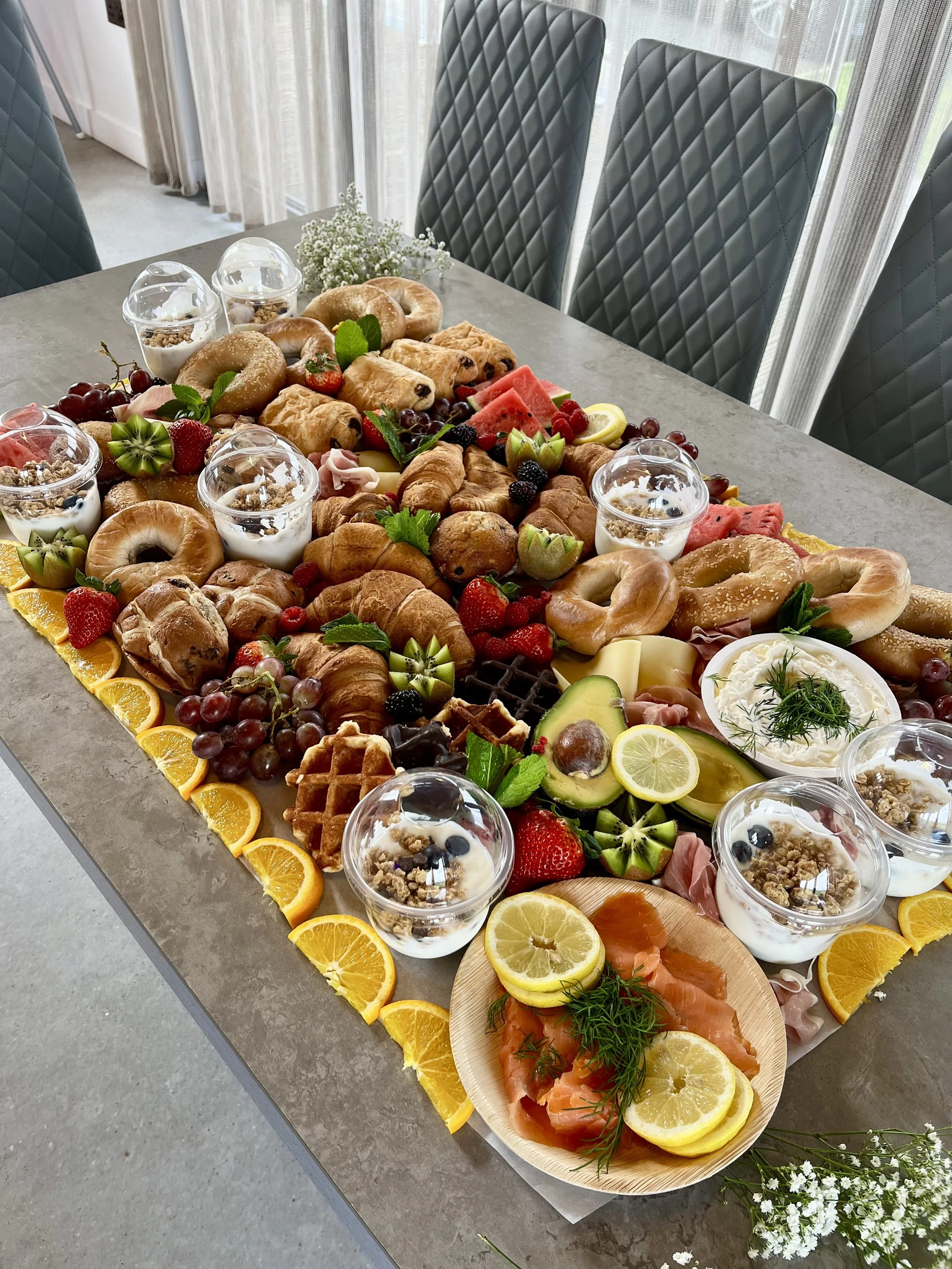 A large spread of assorted cheeses, cured meats, fresh fruits like grapes and figs, crackers, bread, and various dips and spreads on a wooden table for a charcuterie board.
