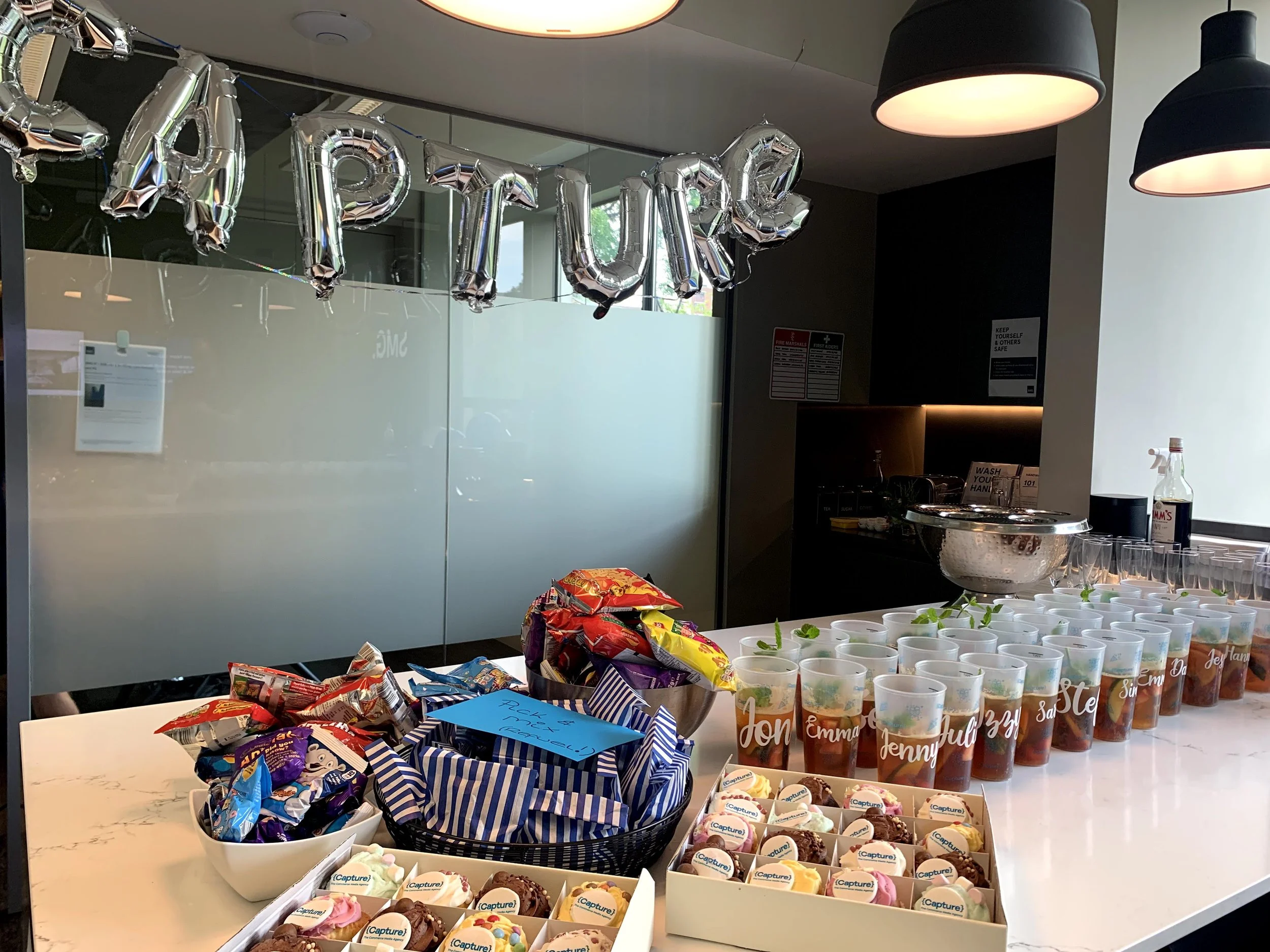 Party setup with snacks and drinks, silver foil balloon letters spelling 'PARTY', cookies in a box, labeled iced tea glasses, and illuminated decor.