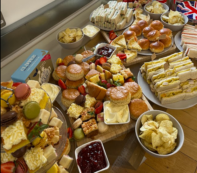A variety of finger foods including sandwiches, scones with clotted cream and jam, potato chips, and assorted desserts on a large table, ready for a gathering or afternoon tea.