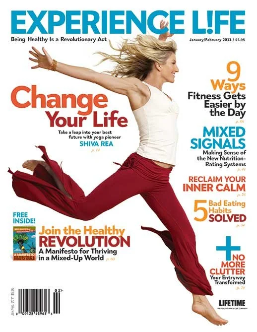 Cover of Experience Life magazine featuring a woman jumping with arms stretched out, wearing a white top and red pants. The magazine title is at the top in blue, with headlines about health, fitness, nutrition, and lifestyle.