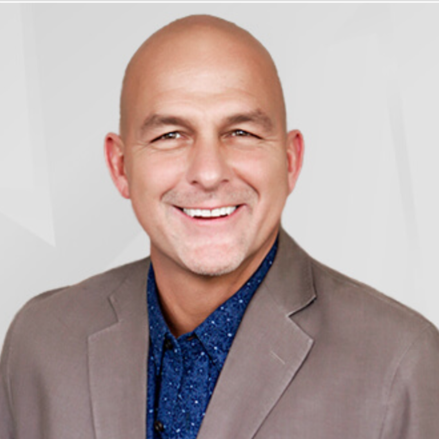 Headshot of a smiling bald man wearing a gray blazer and a blue patterned shirt