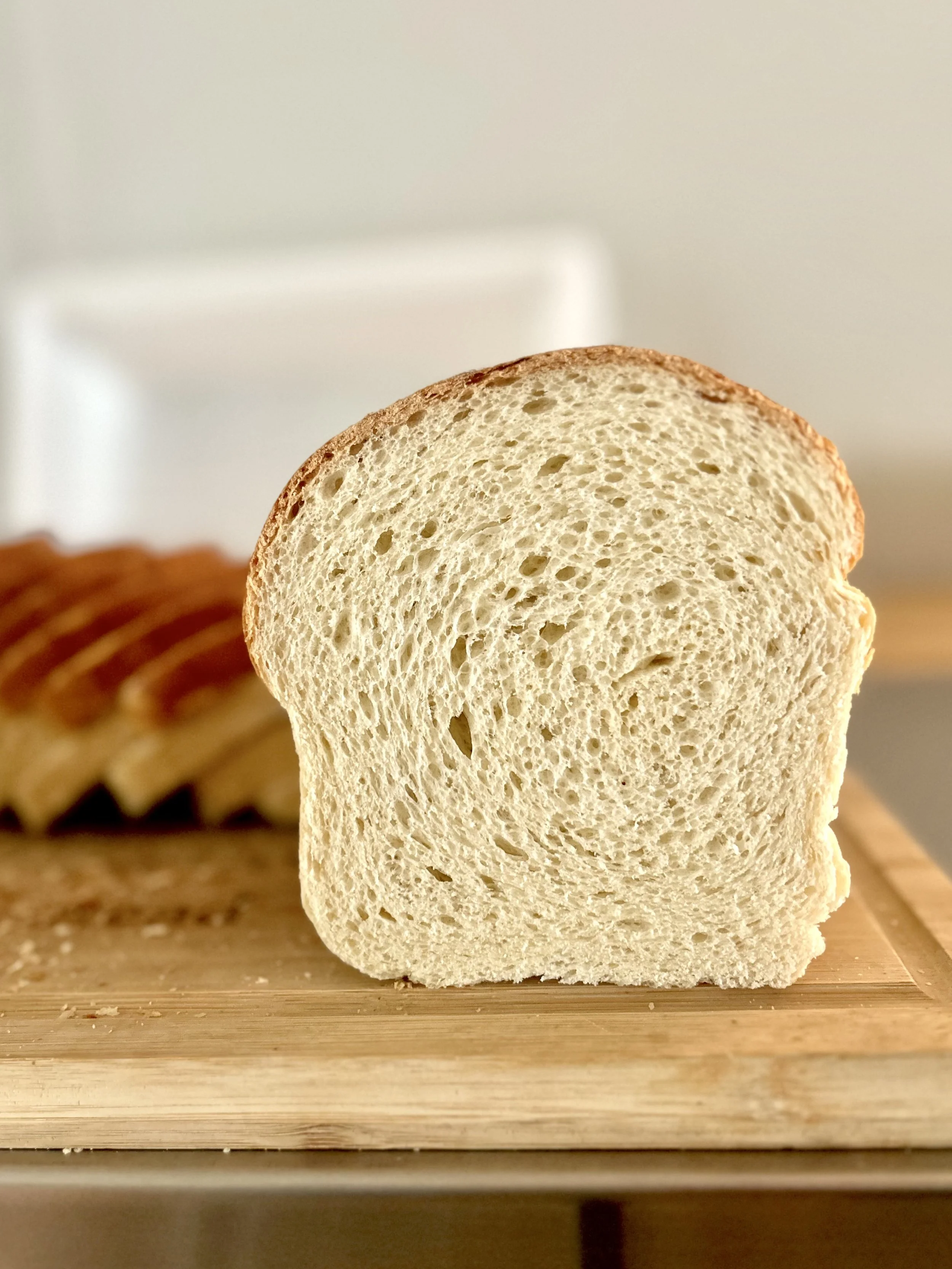 The best homemade sandwich bread. Close-up of a slice of white bread on a wooden cutting board with more bread slices blurred in the background. Knead and Grow Homestead uses mindful ingredients, seed oil free. Our sandwich bread is seed oil free.