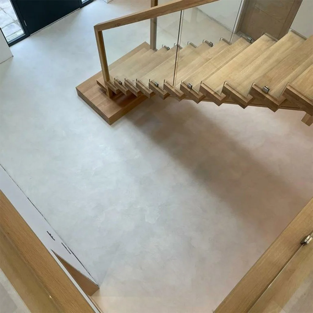 Top-down view of a staircase with wooden steps and glass railing, leading down to a light-colored floor in a modern building.