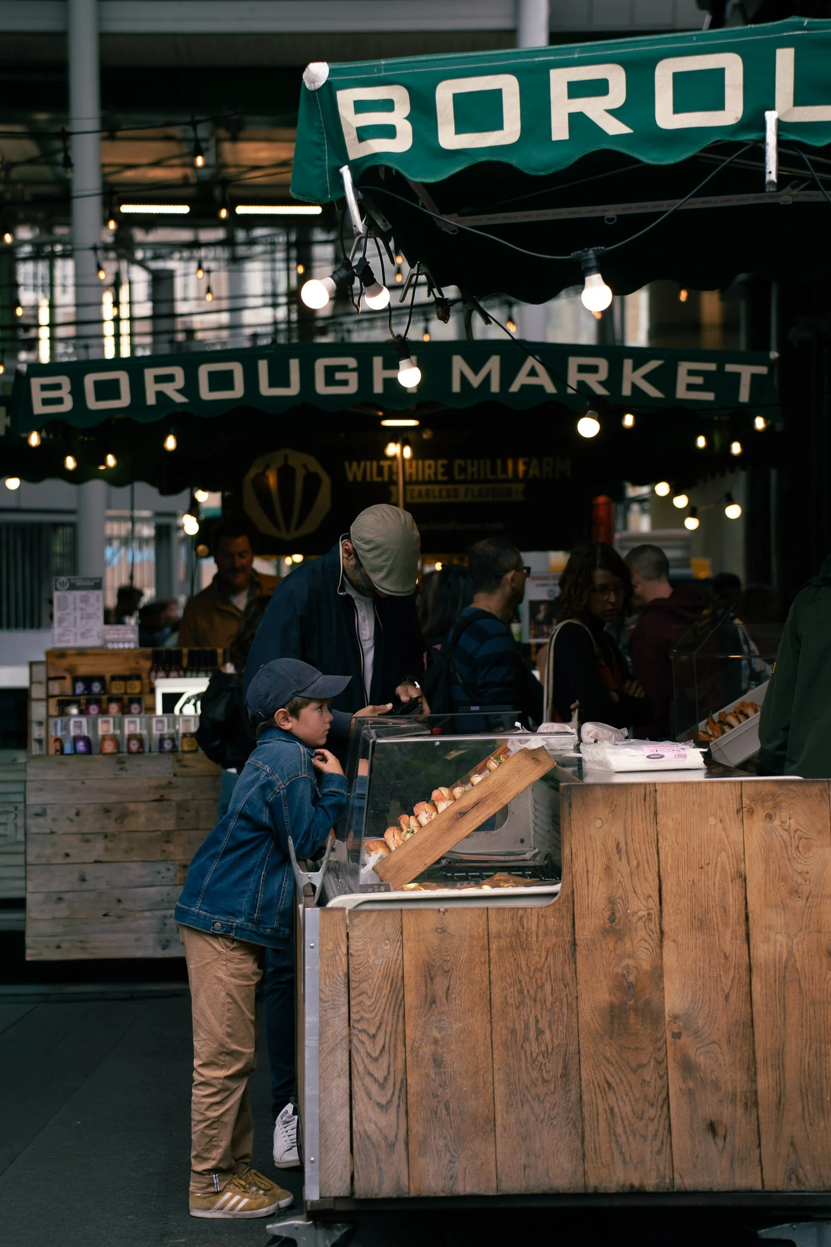 People shopping at a market stall with a sign that reads 'Borough Market', featuring a young boy and adults ordering food.