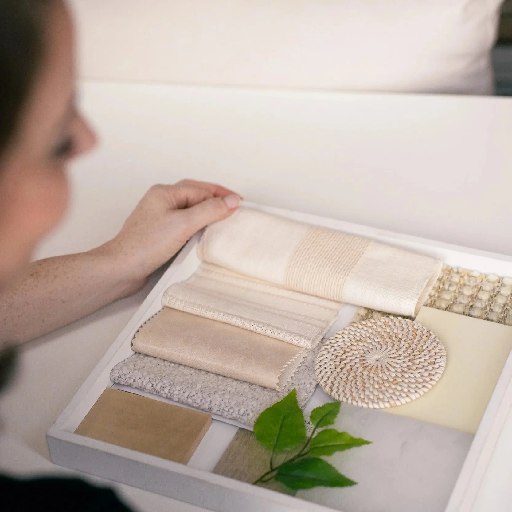 Sample display of fabric swatches, textile textures, and natural woven items arranged on a board, with a person's hand touching the textiles.