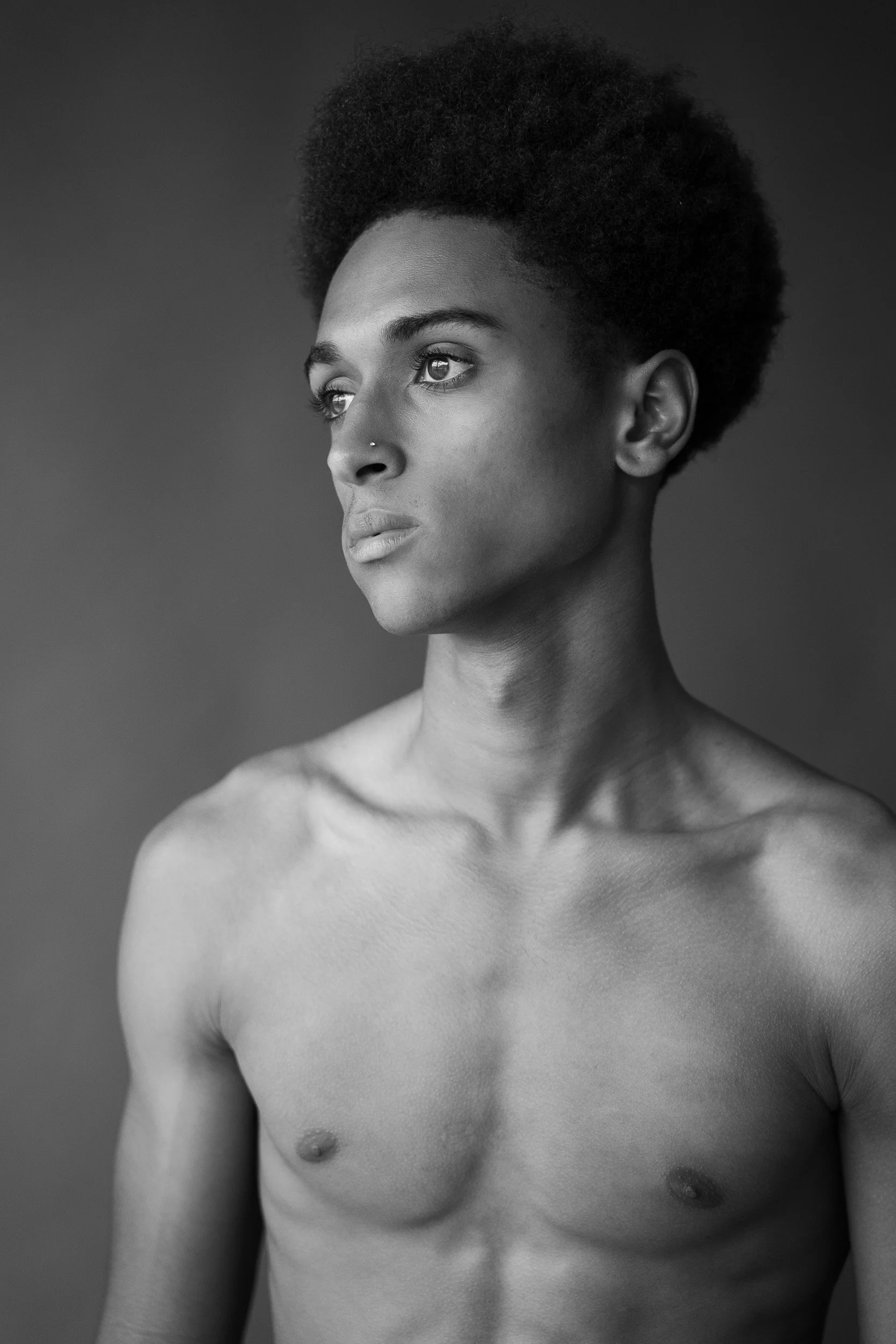 Black and white portrait of a young woman with short curly hair, looking thoughtfully to the side, with bare shoulders and chest, against a plain background.