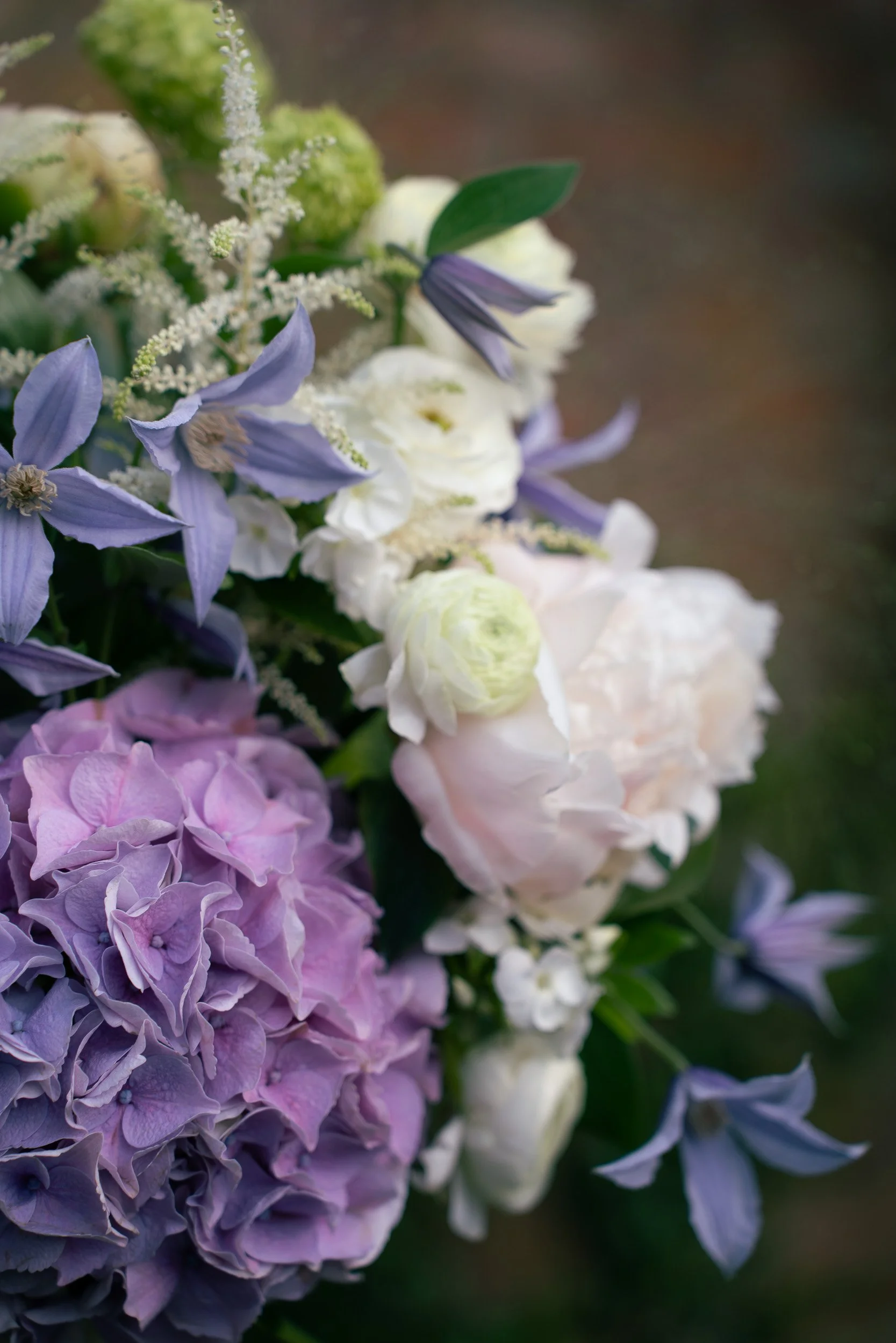 Close-up of a bouquet of white, purple, and light pink flowers with green leaves.