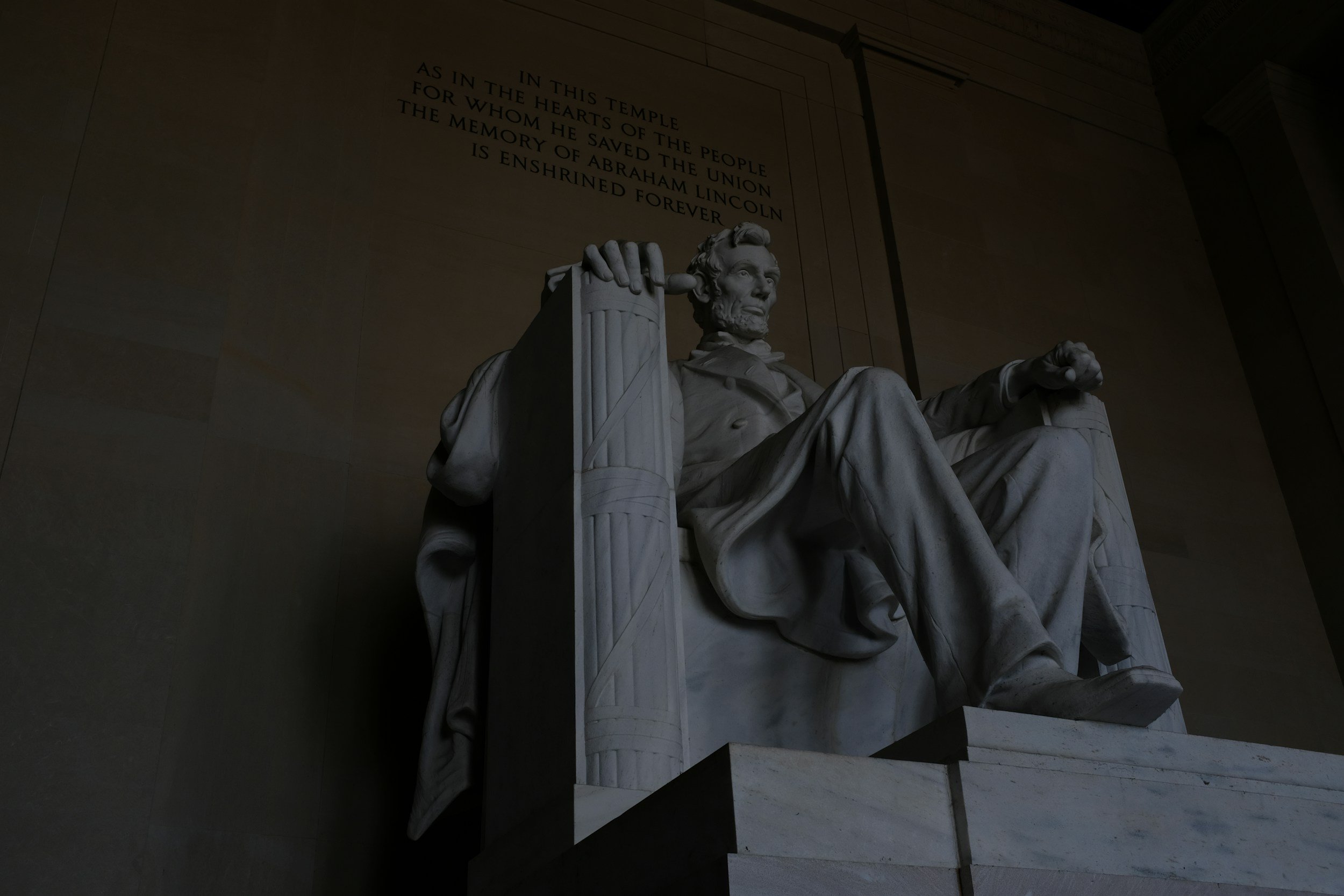 Dark, moody photo of the Lincoln Memorial, with an inscription on the wall behind him.