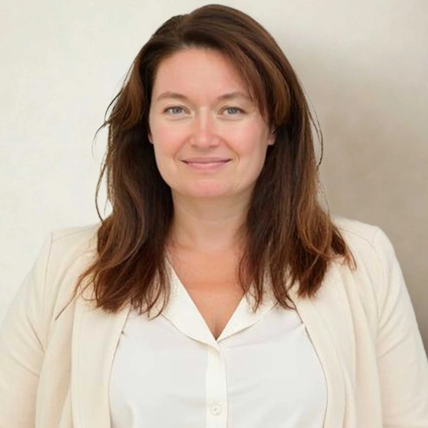 A woman with shoulder-length brown hair wearing a white blazer and blouse, smiling against a plain light-colored background.