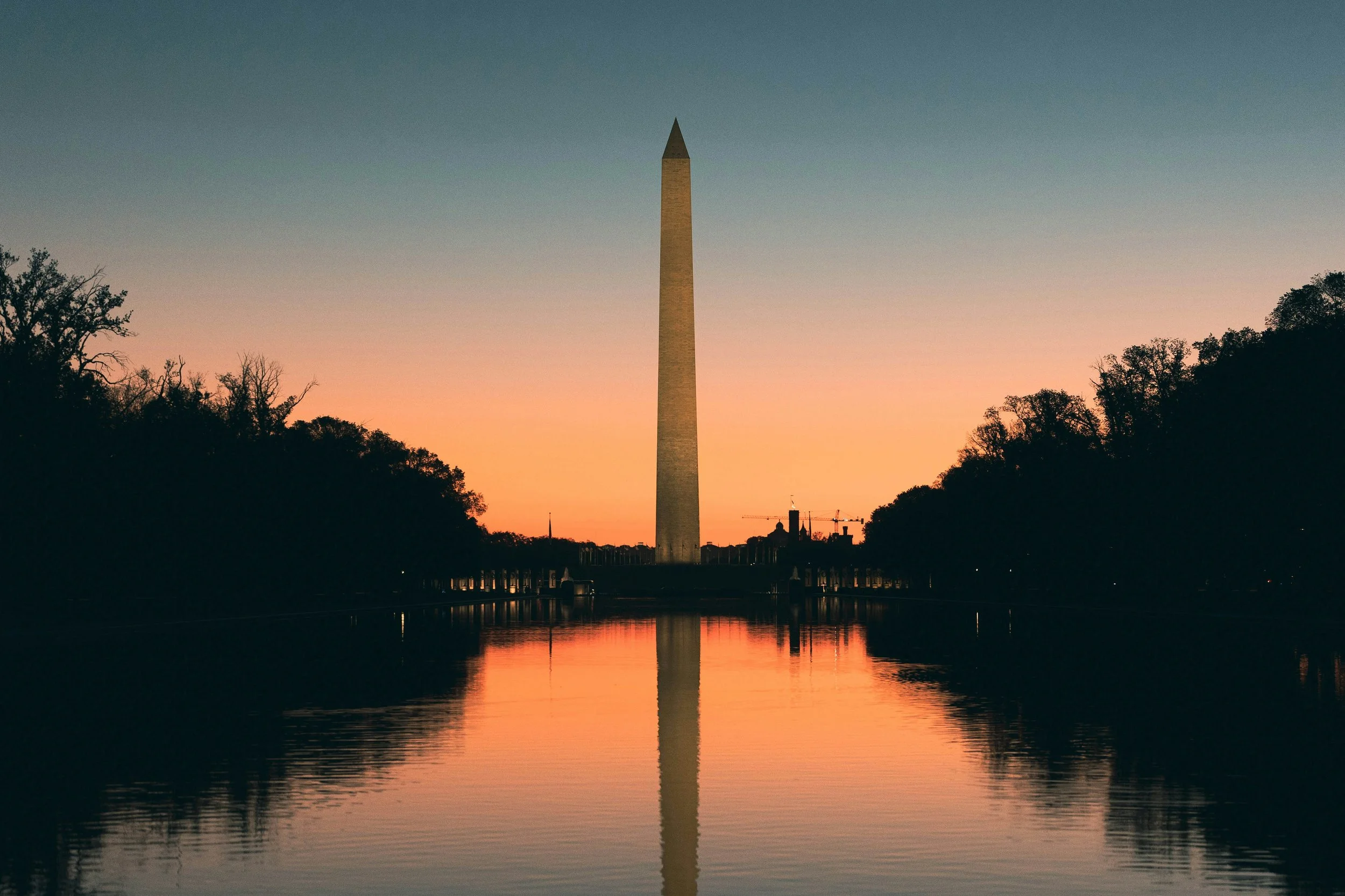Sunset over the Washington Monument reflecting on a calm waterway with trees on both sides.