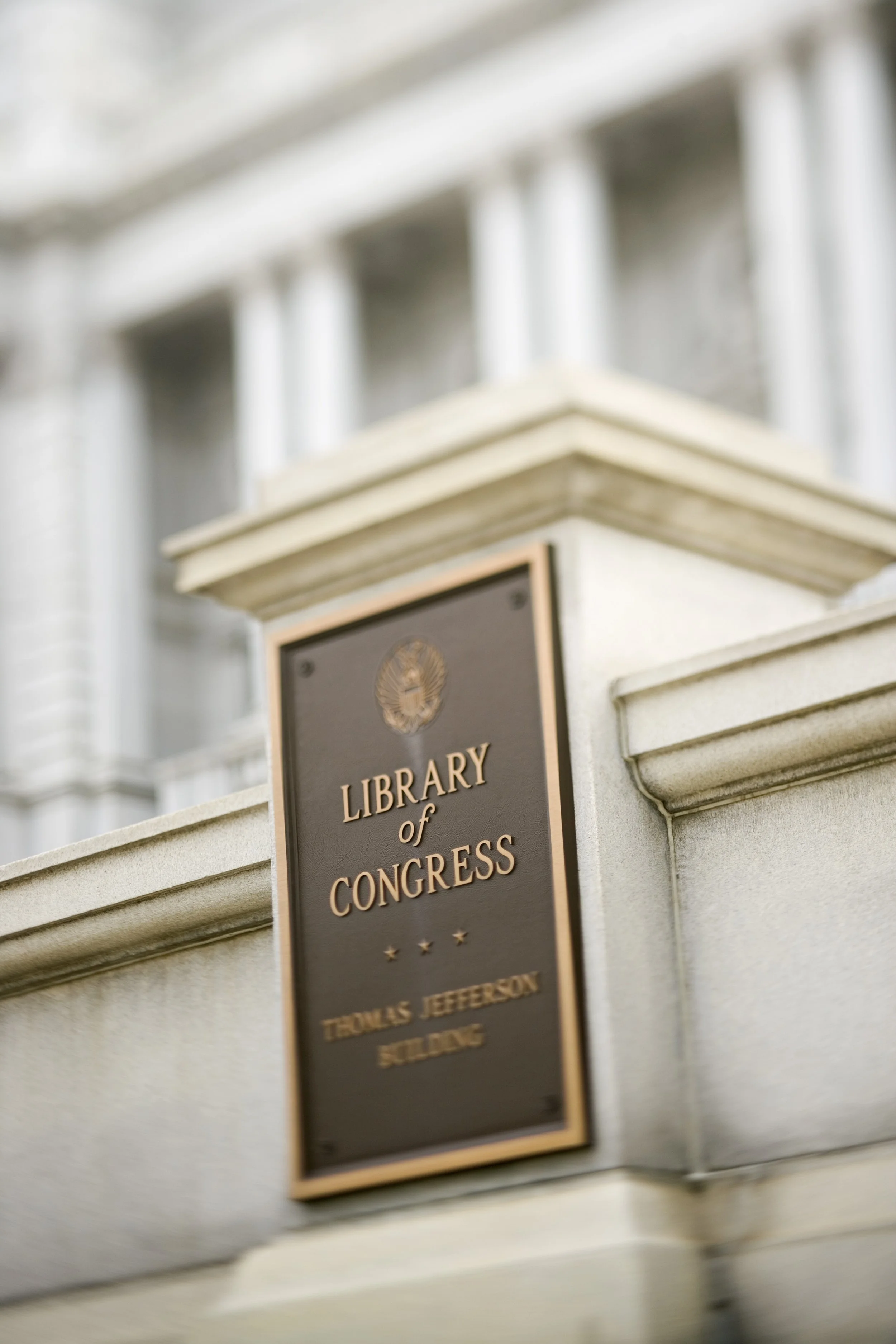 Close-up of a bronze plaque on a building with the words "Library of Congress" and "Thomas Jefferson Building," mounted on a beige stone wall.