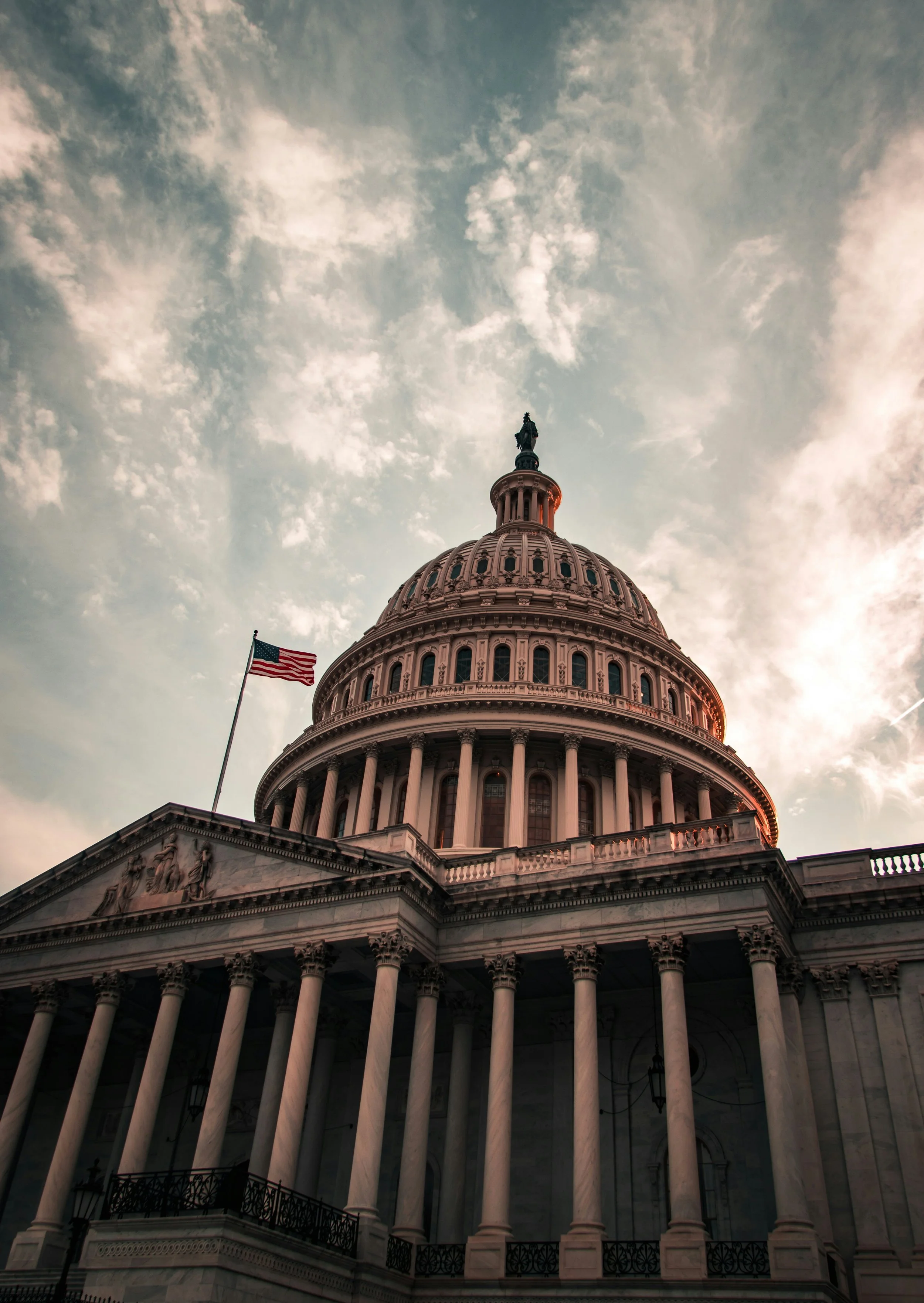 The United States Capitol building with an American flag, under a partly cloudy sky during sunset.