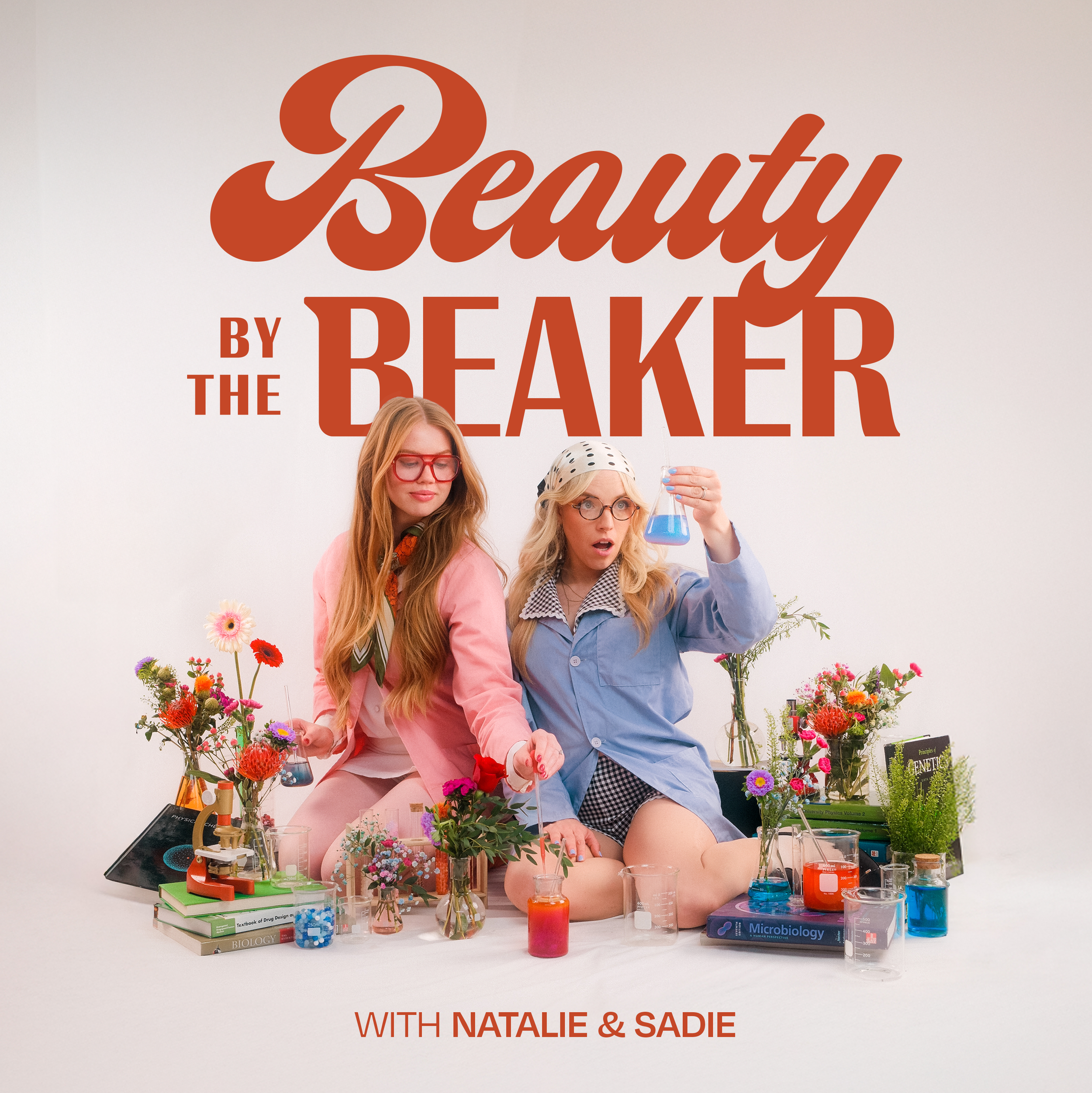 Two women in colorful vintage clothing surrounded by flowers and science lab equipment, sitting on the floor with a white background. The large text above them reads 'Beauty by the Beaker' and smaller text below says 'with Natalie & Sadie'.