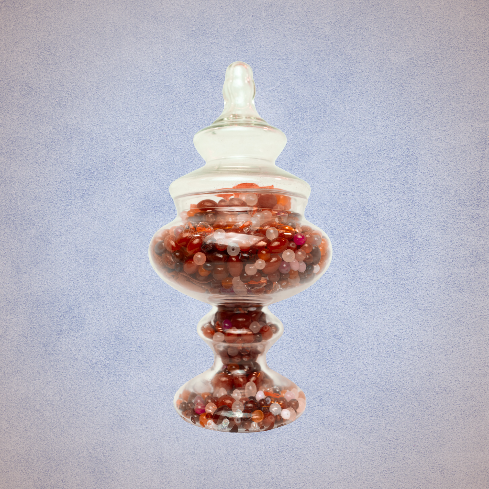 A glass decorative jar filled with multicolored beads, set against a textured light blue background.