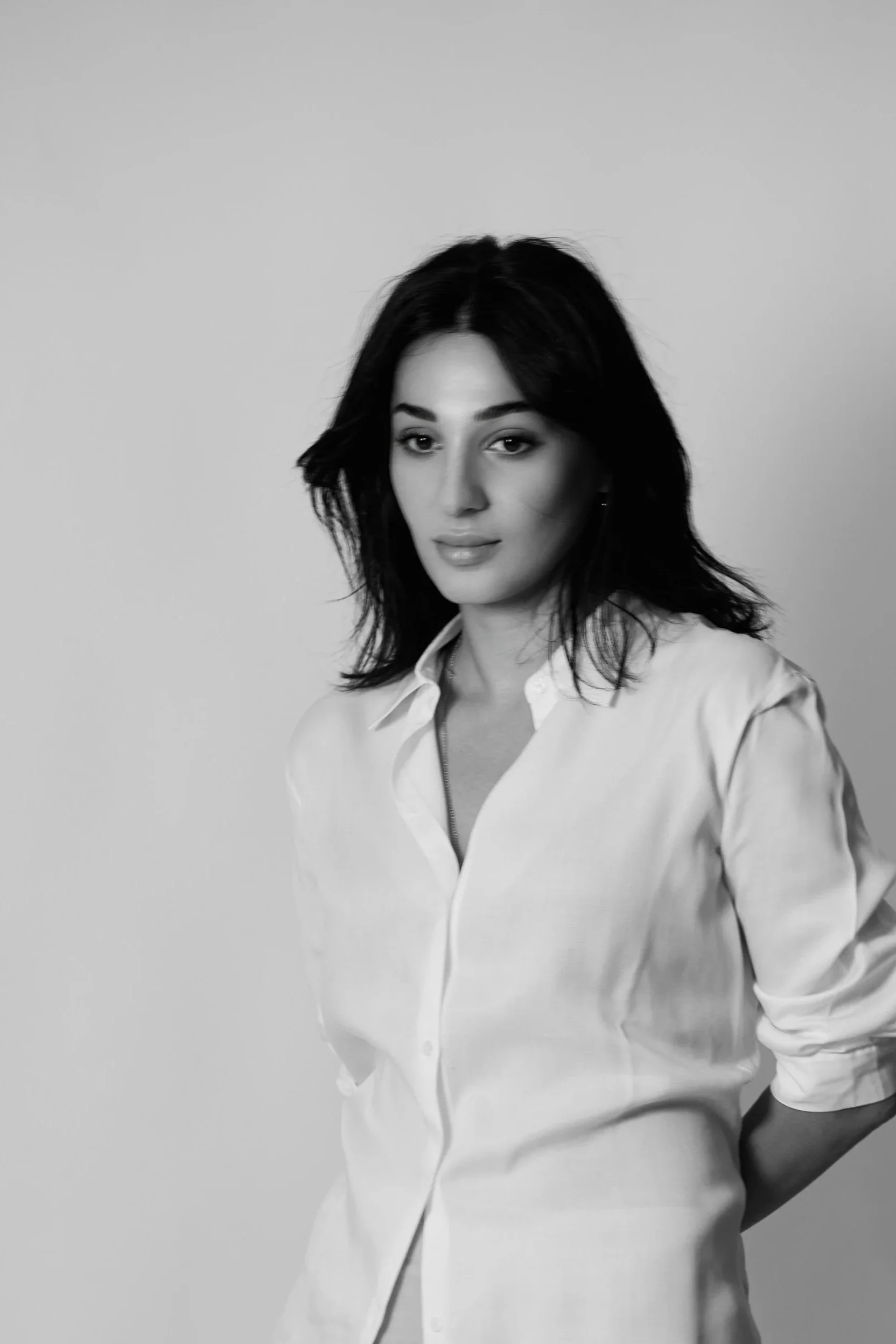 Black and white portrait of a woman with dark hair wearing a button-up shirt, standing against a plain background.