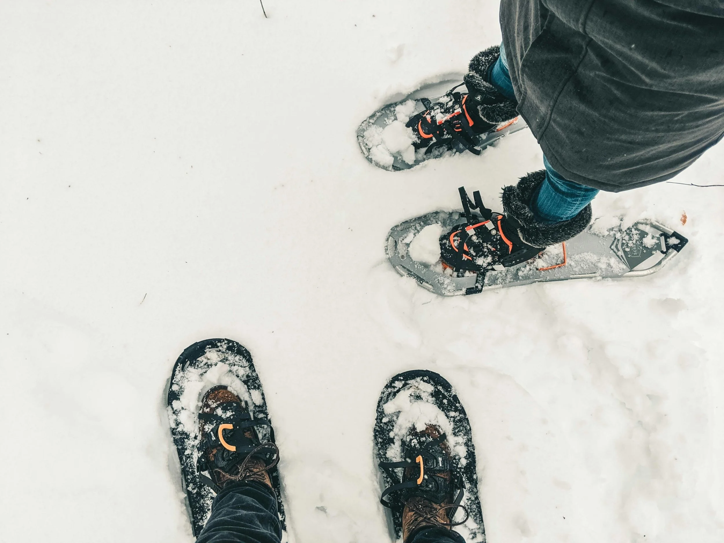 Two people wearing snowshoes standing on snow, viewed from above.