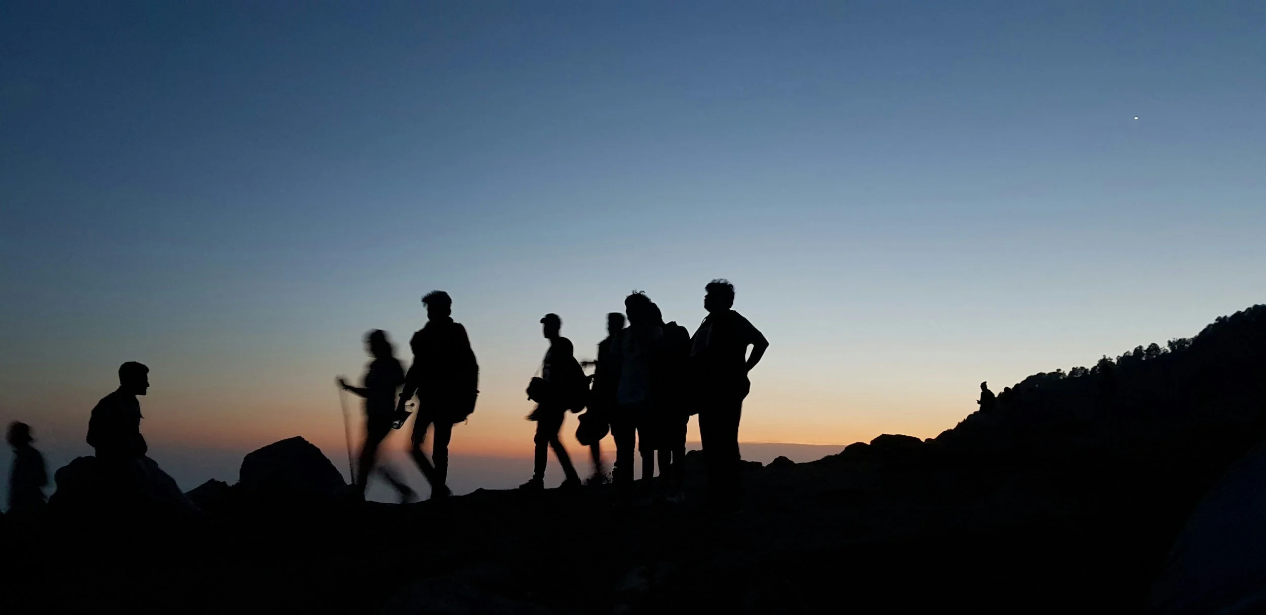 Silhouettes of people hiking on a mountain during sunset with a clear sky and a star visible.
