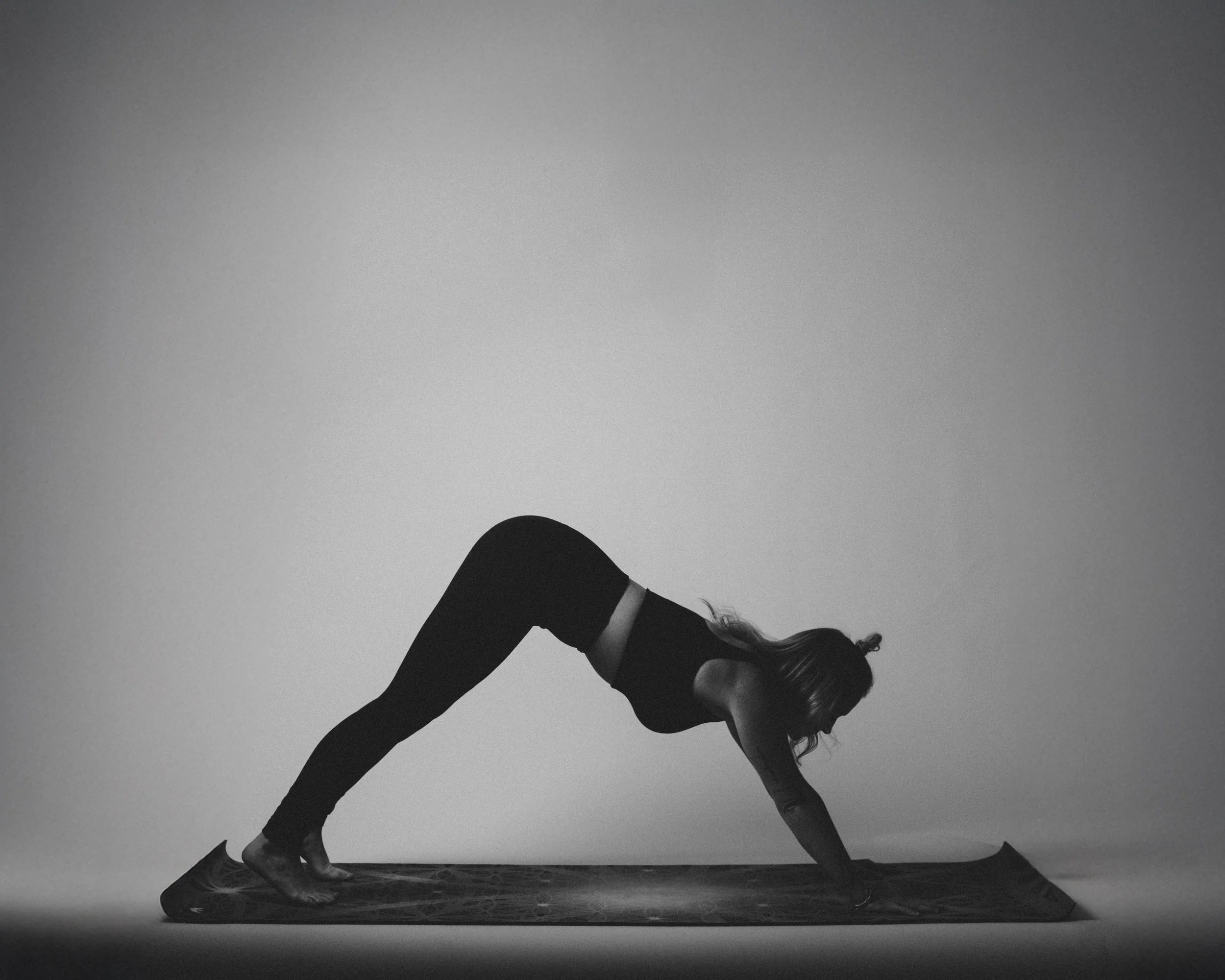 A woman practicing yoga on a mat in a plank pose against a plain background.
