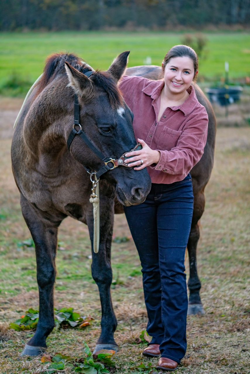 Dr. Jessica Tyndall of Bouncing Back Chiropractic standing next to a brown horse with a black mane, one of her mobile equine chiropractic patients.
