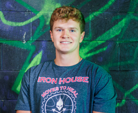A young man with curly red hair and a blue t-shirt standing in front of a colorful graffiti wall.