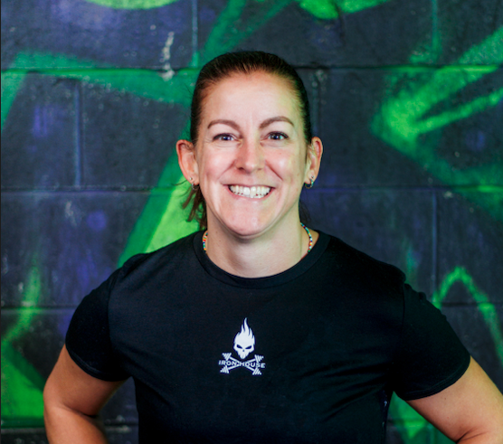 A woman smiling in front of a graffiti wall, wearing a black T-shirt with a white logo.