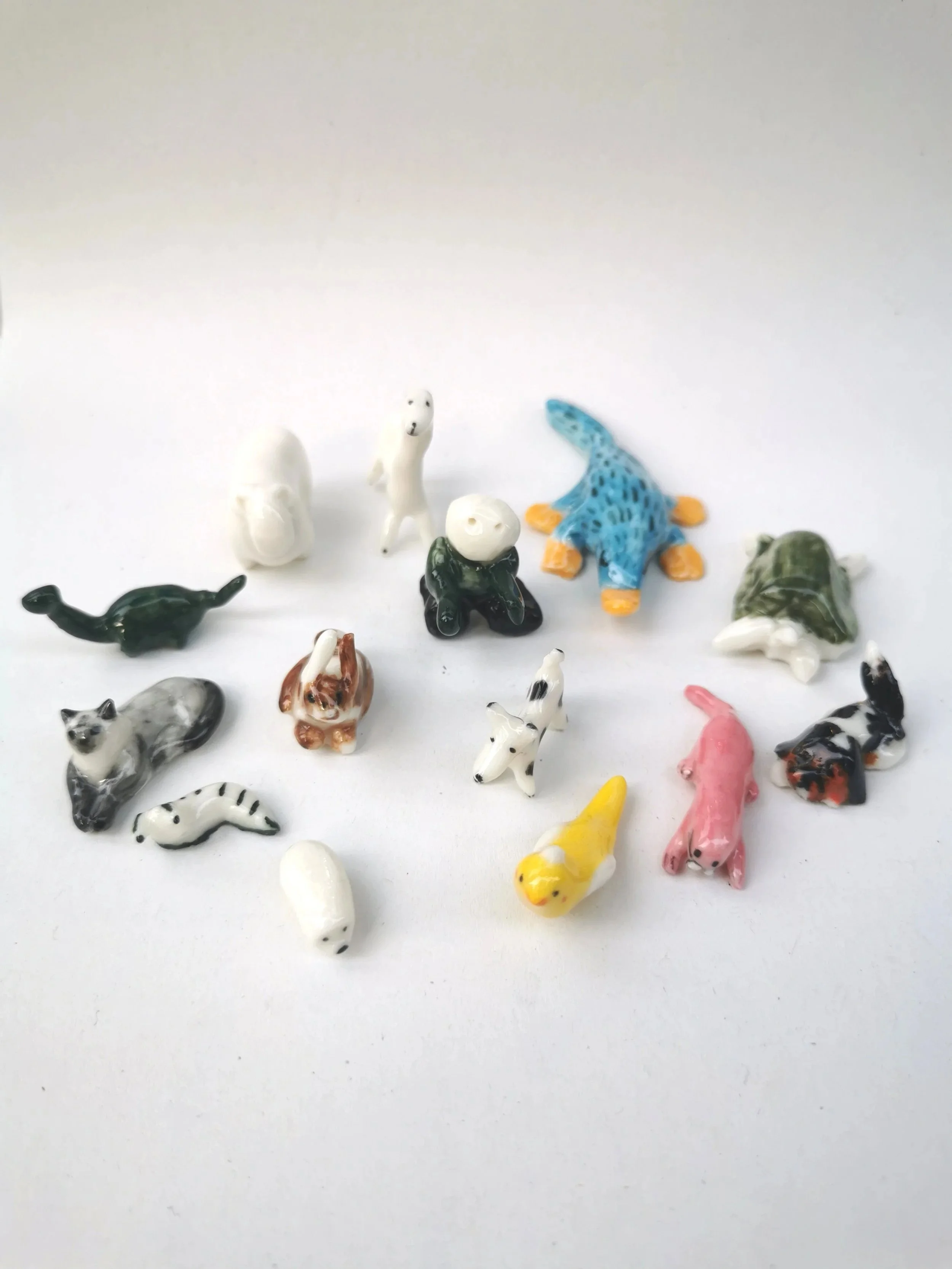 Collection of small, colorful toy animal figurines including dogs, cats, a horse, a duck, a turtle, a crocodile, and a whale, arranged on a white surface.