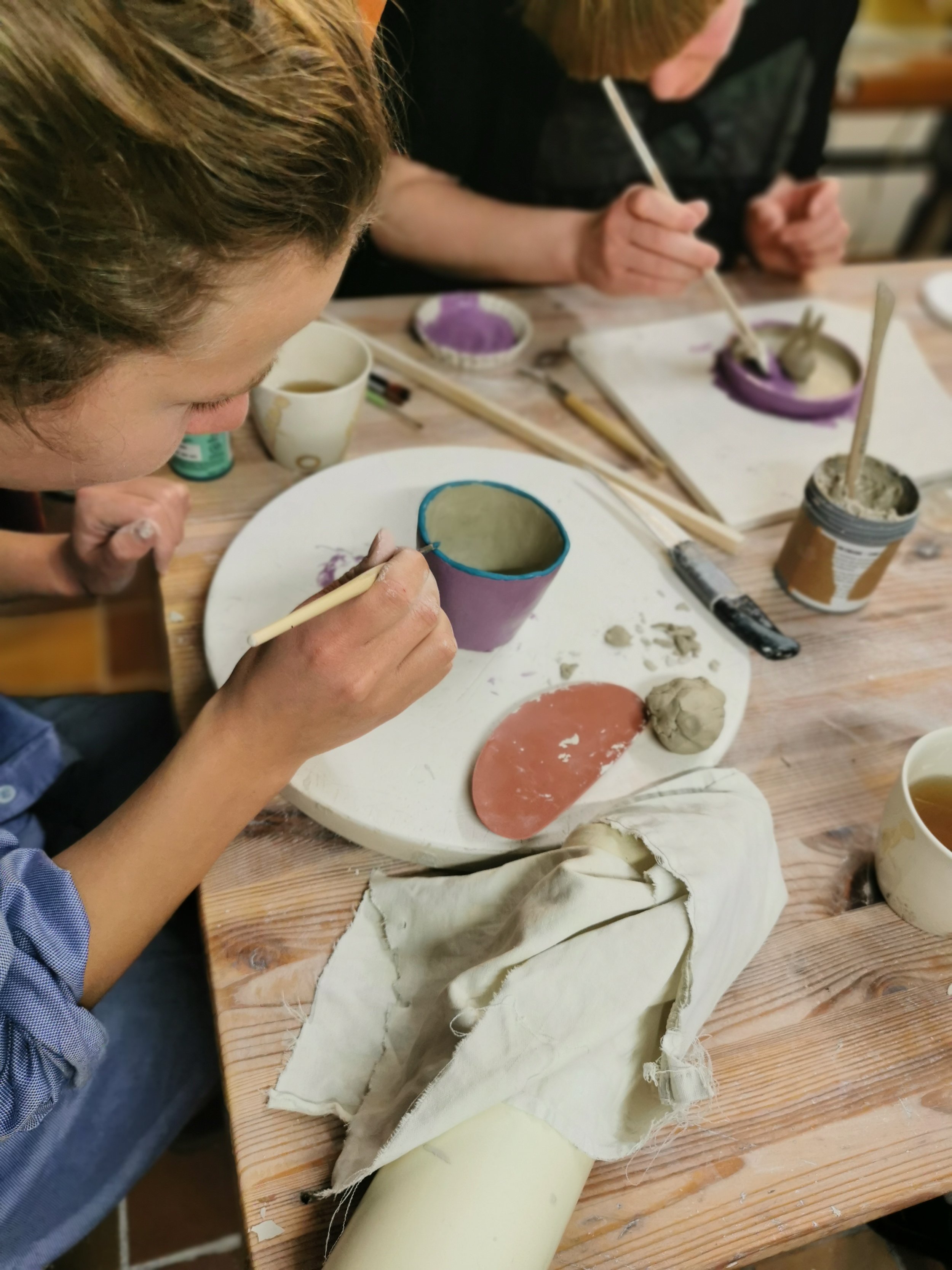 People painting pottery with brushes and colorful glazes at a wooden table.