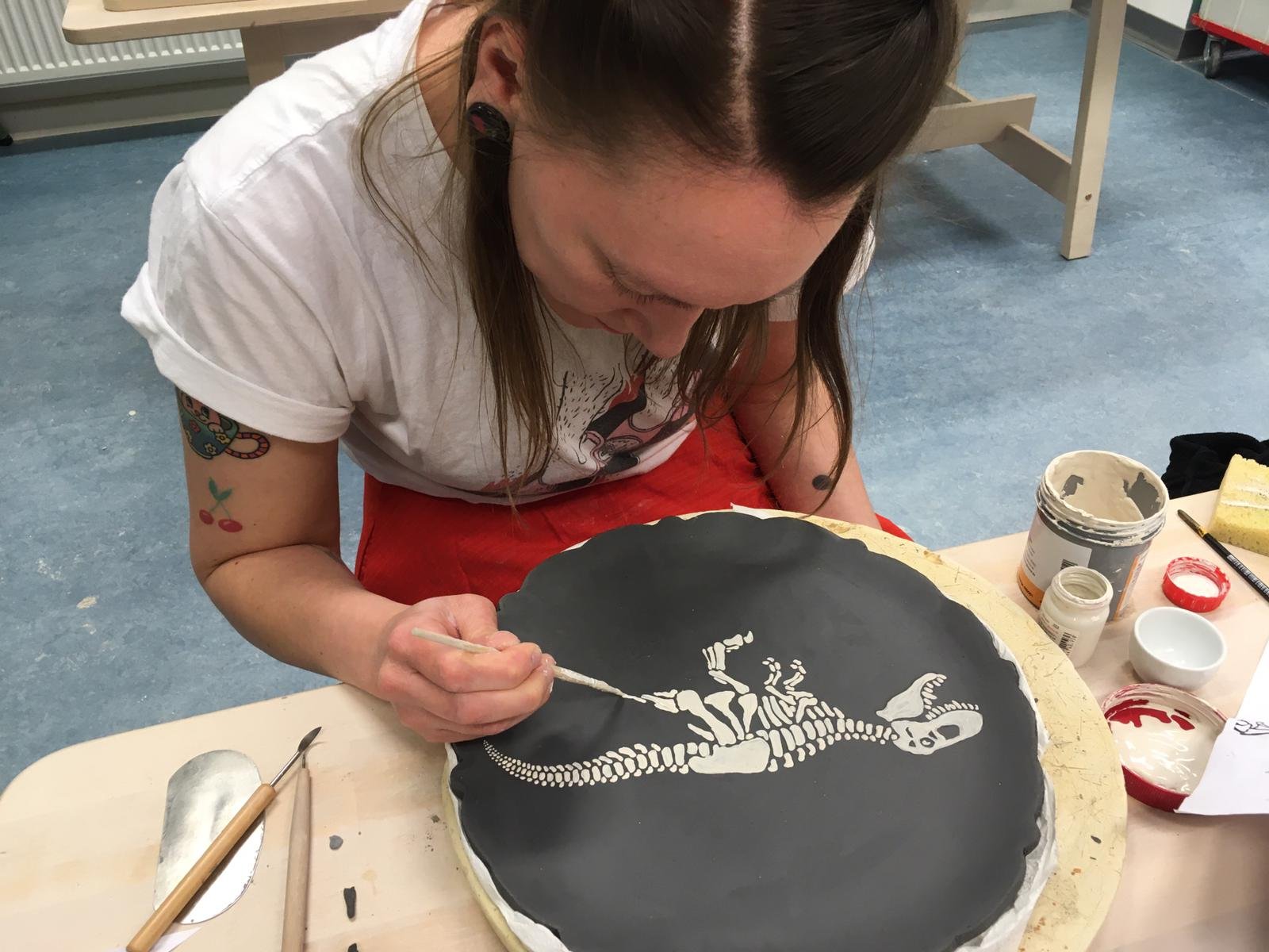 A woman painting a skeleton on a black circular surface in an art studio.