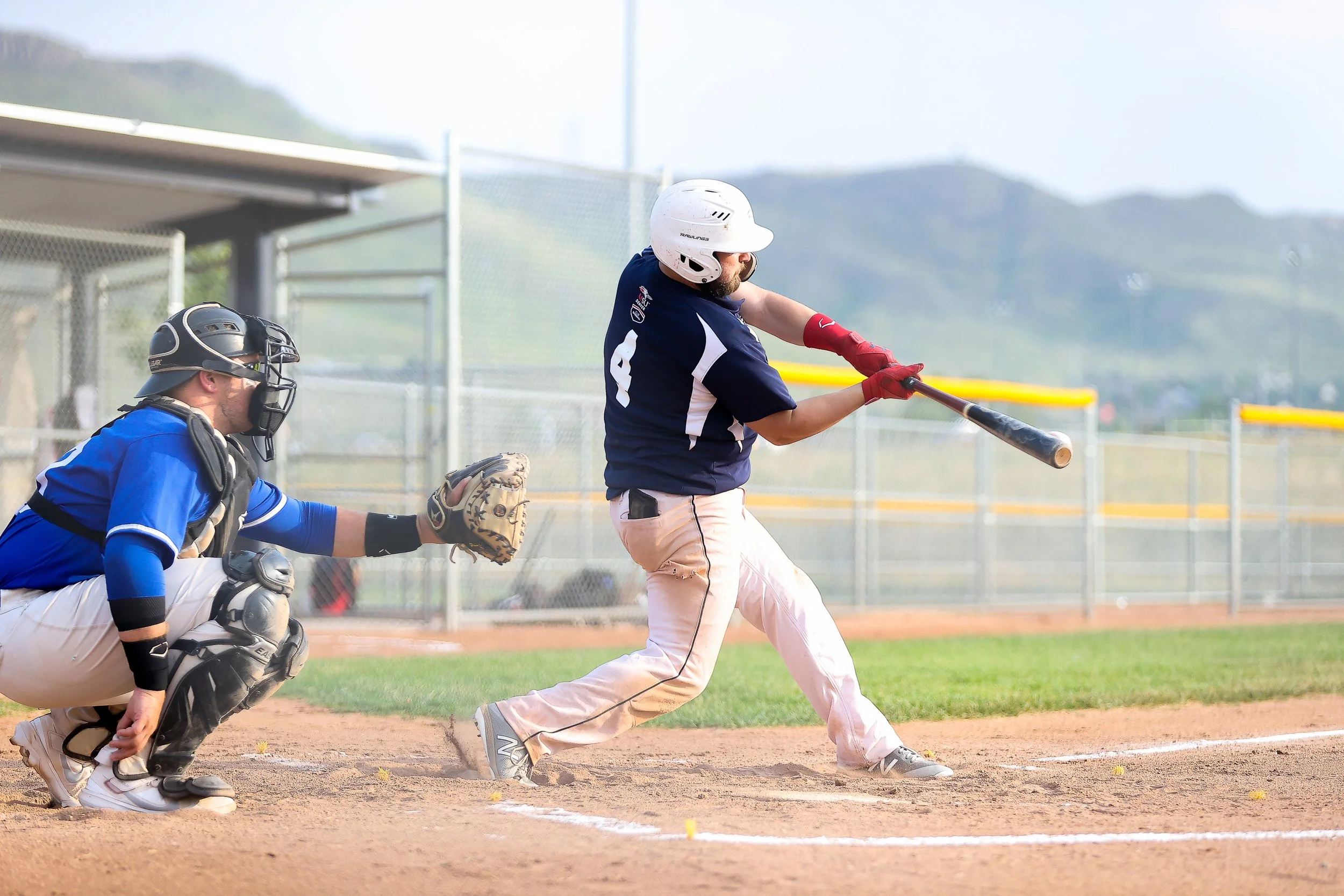A baseball player swinging a bat at a pitched ball during a game with an umpire crouching behind him in protective gear.