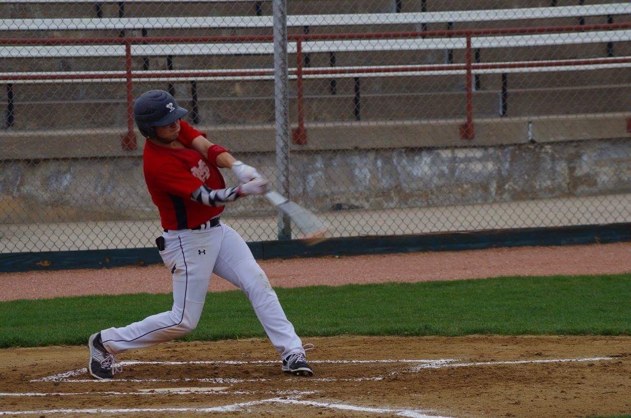 A baseball player in a red jersey and white pants swinging a bat at a pitched ball on a baseball field.