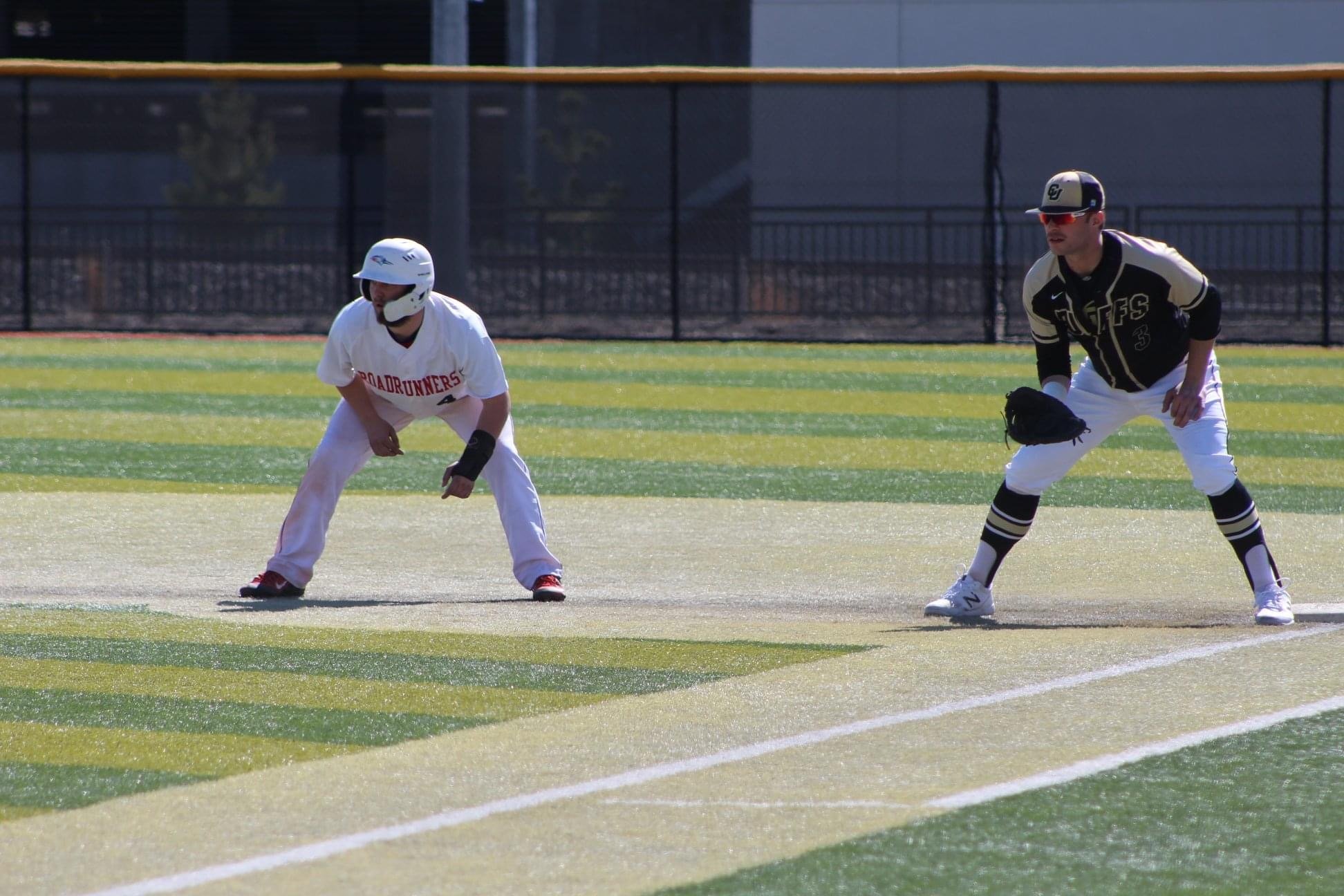 Two baseball players crouching on a field, ready for a play, with a black fence in the background.