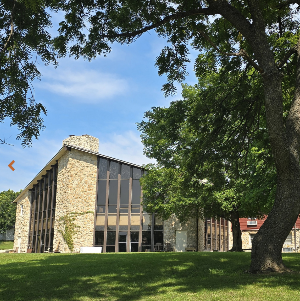 A large stone and glass building surrounded by green trees and grass under a blue sky.