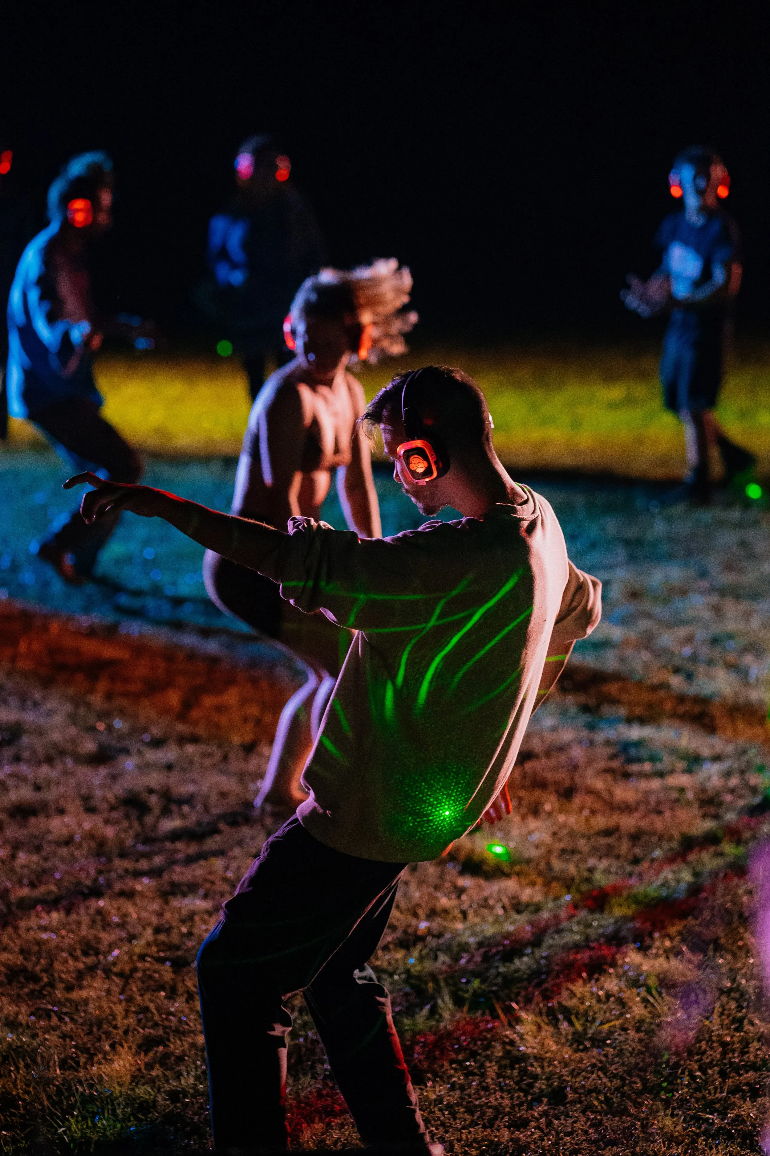 People dancing and having fun outdoors at night under colorful lights, some wearing headphones.
