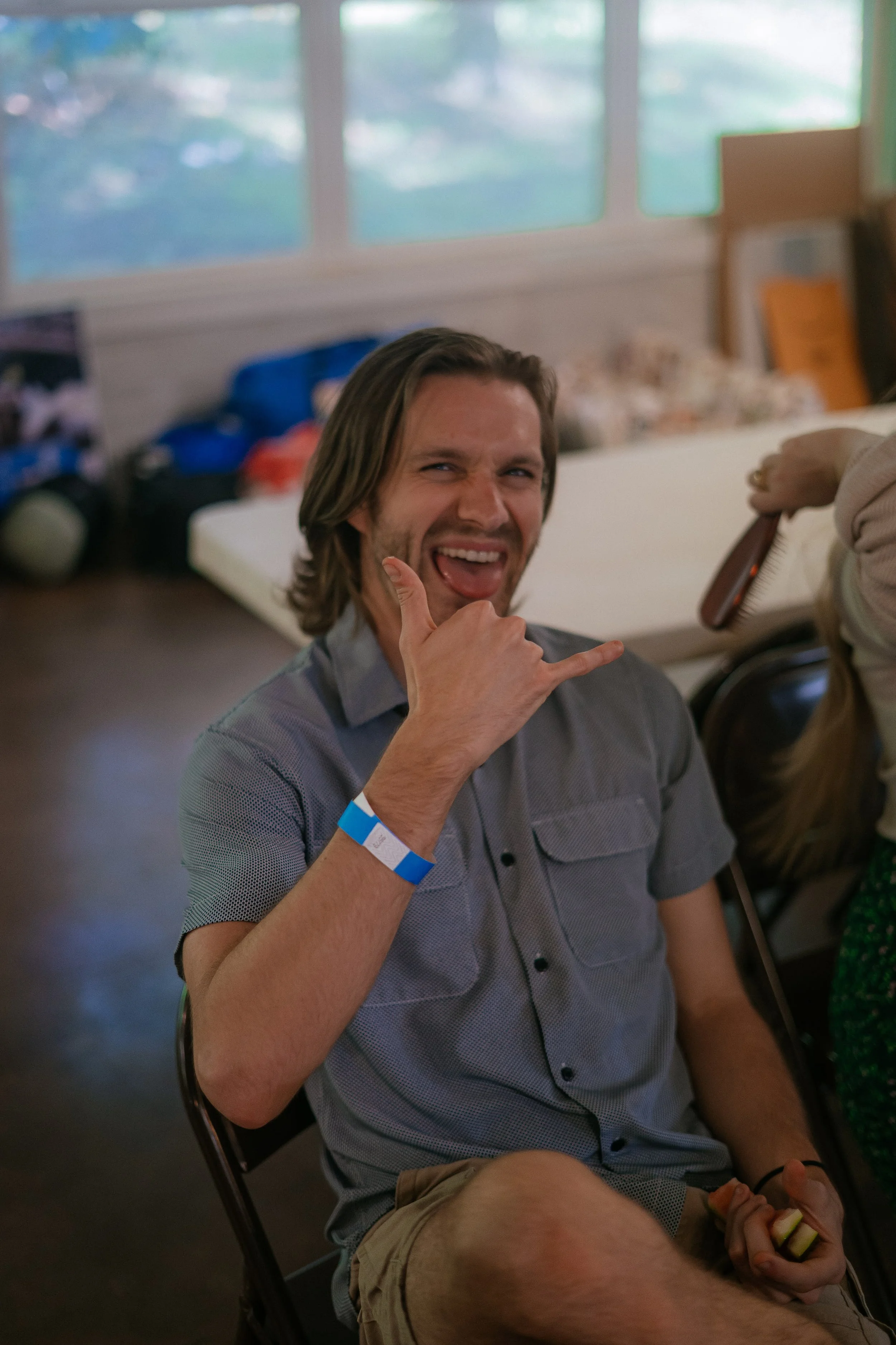 A man sitting on a chair making a rock and roll gesture with his hand, smiling with his tongue out.